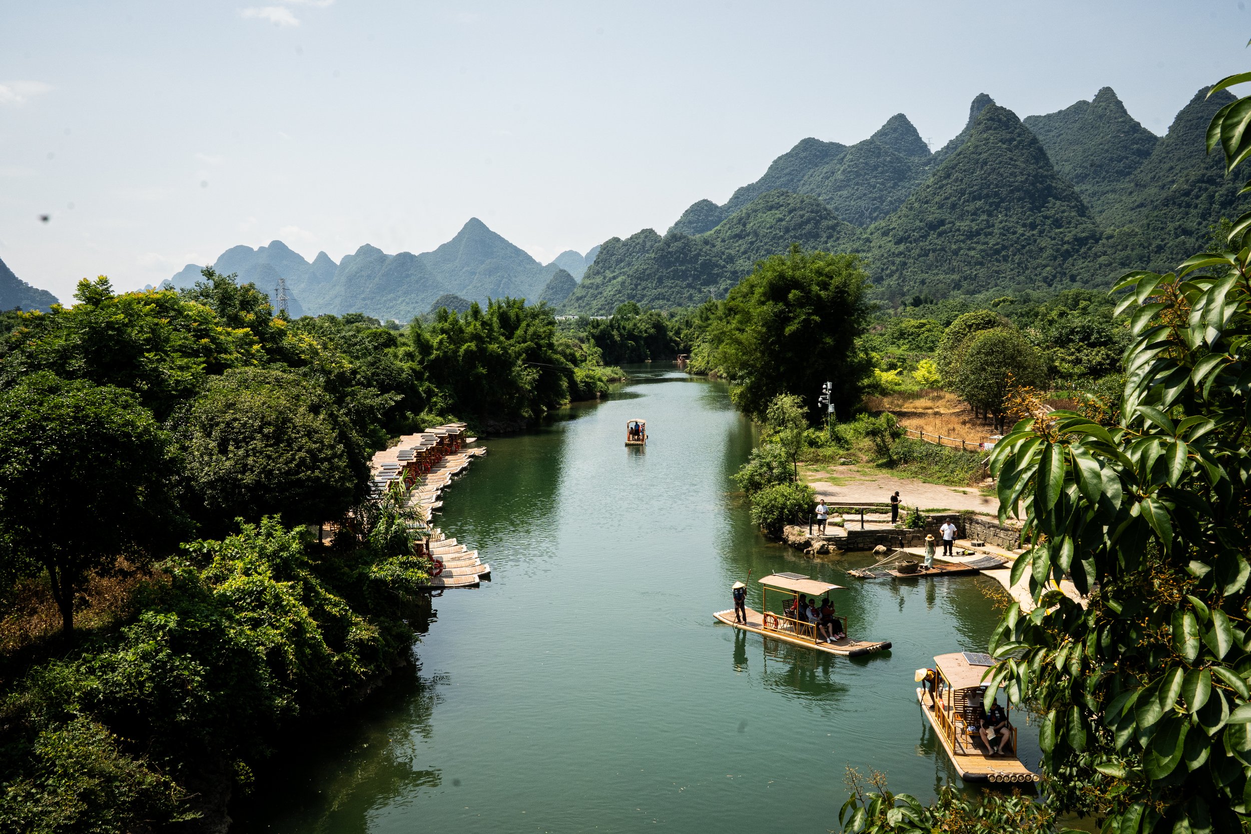 Rivière entourée de verdure avec montagnes karstiques en arrière-plan et bateaux en bois transportant des touristes sur l'eau.