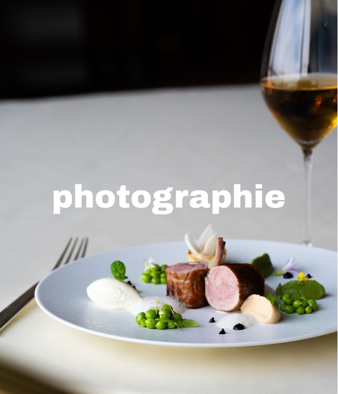 Plat sophistiqué avec viande, pois verts, et garnitures, accompagné d'un verre de vin blanc ou rosé, sur une nappe blanche, avec des couverts sur le côté.