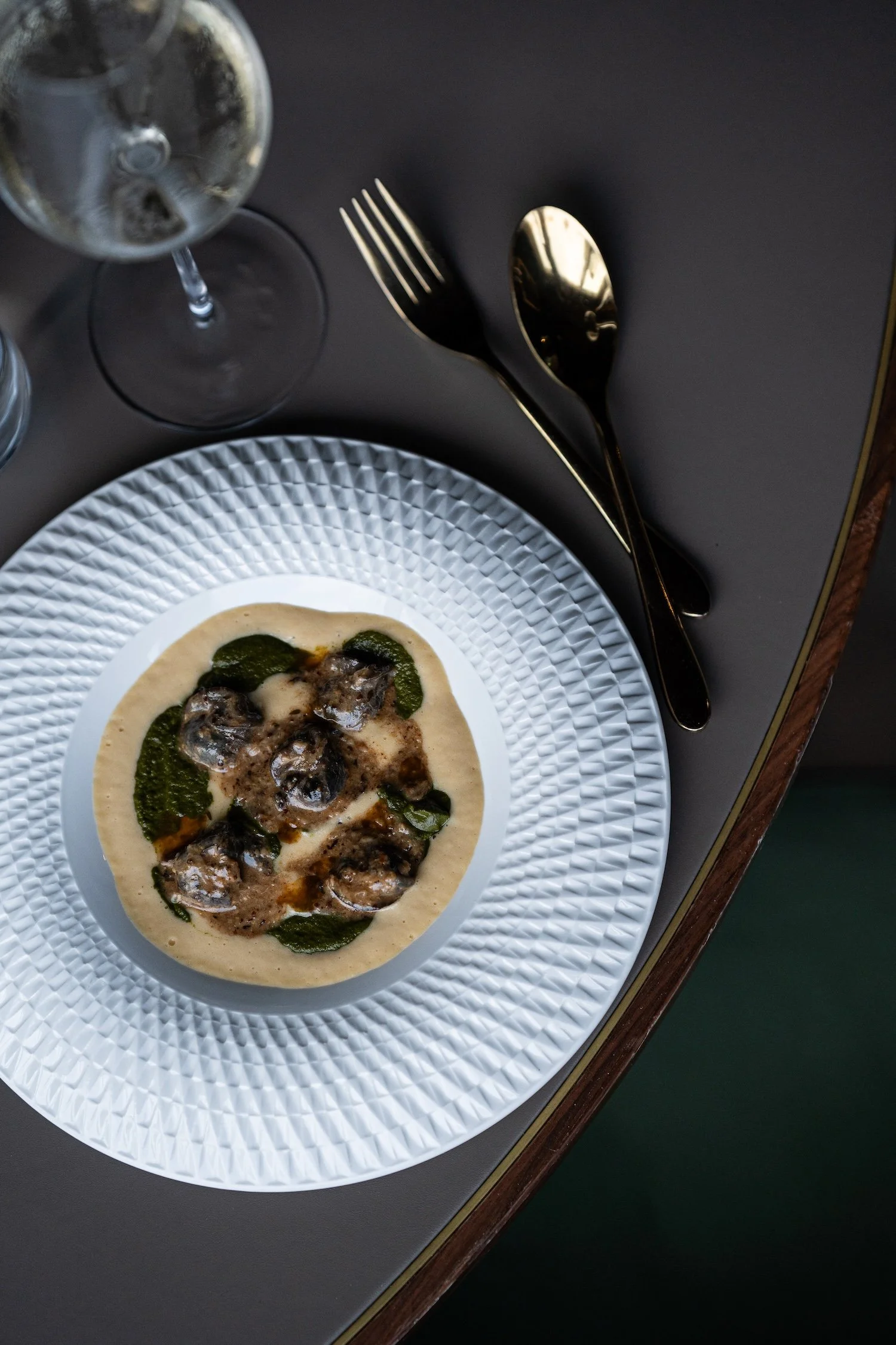Une assiette de pizza avec des champignons, du pesto et du fromage, accompagnée d'une fourchette et d'une cuillère en argent, vue du dessus sur une table noire.