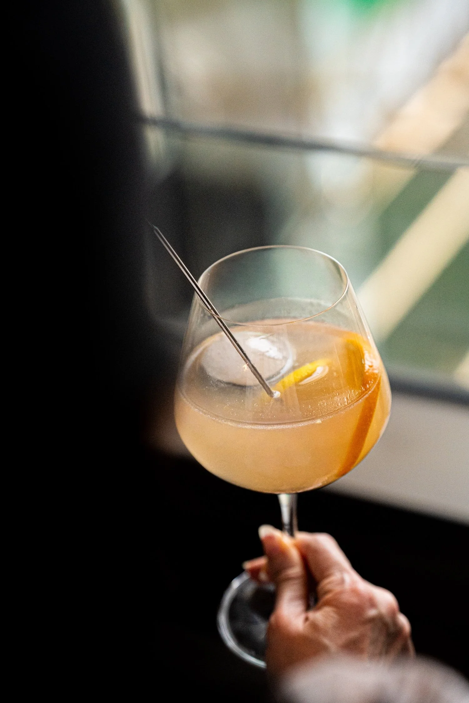 Verre à cocktail orange avec une tranche d'orange, contenant une boisson, tenu par une main