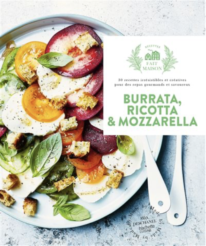 Une assiette de salade avec des tomates, de la mozzarella, du basilic et des croûtons, accompagnée d'un livre de cuisine sur les recettes de burrata, ricotta et mozzarella.