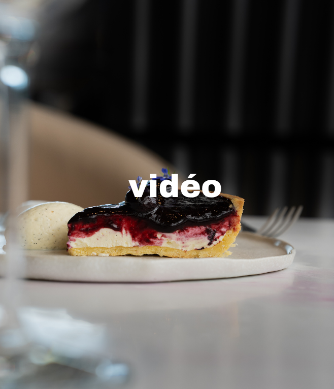 Une part de tarte aux fruits rouges avec une boule de glace à côté, présentée sur une assiette blanche, sur une table dans un restaurant.