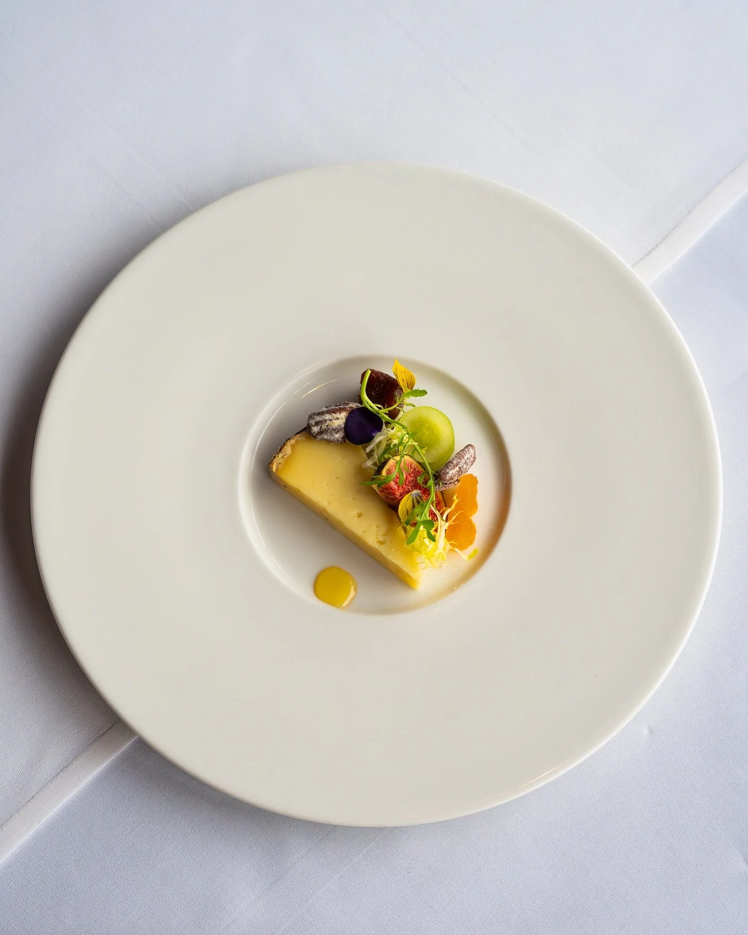 Dessert à base de fromage ou cheesecake avec des fruits et des fleurs comestibles, présenté dans une assiette blanche