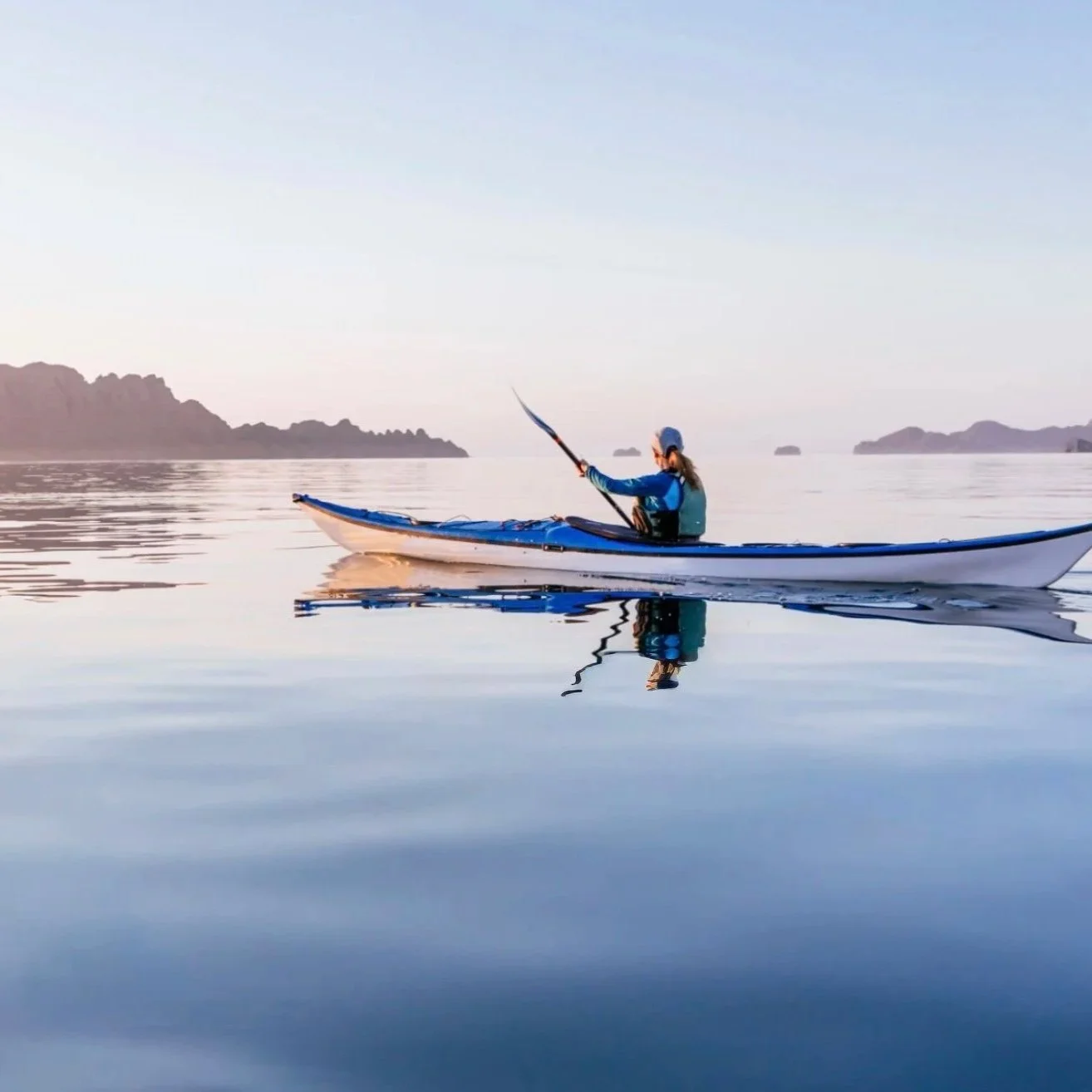 A person kayaking on calm water near distant islands during sunset.
