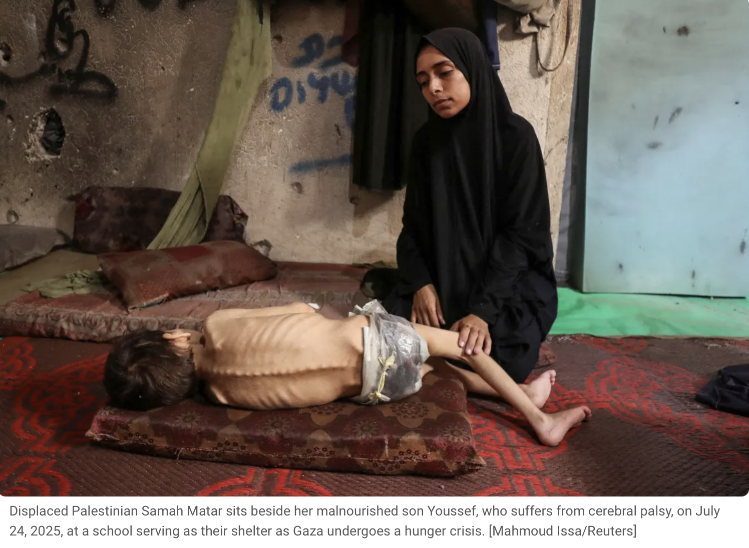 A young girl dressed in black clothing sits beside a malnourished boy lying on a mat inside a shelter, with a worn wall and a partially open door in the background.