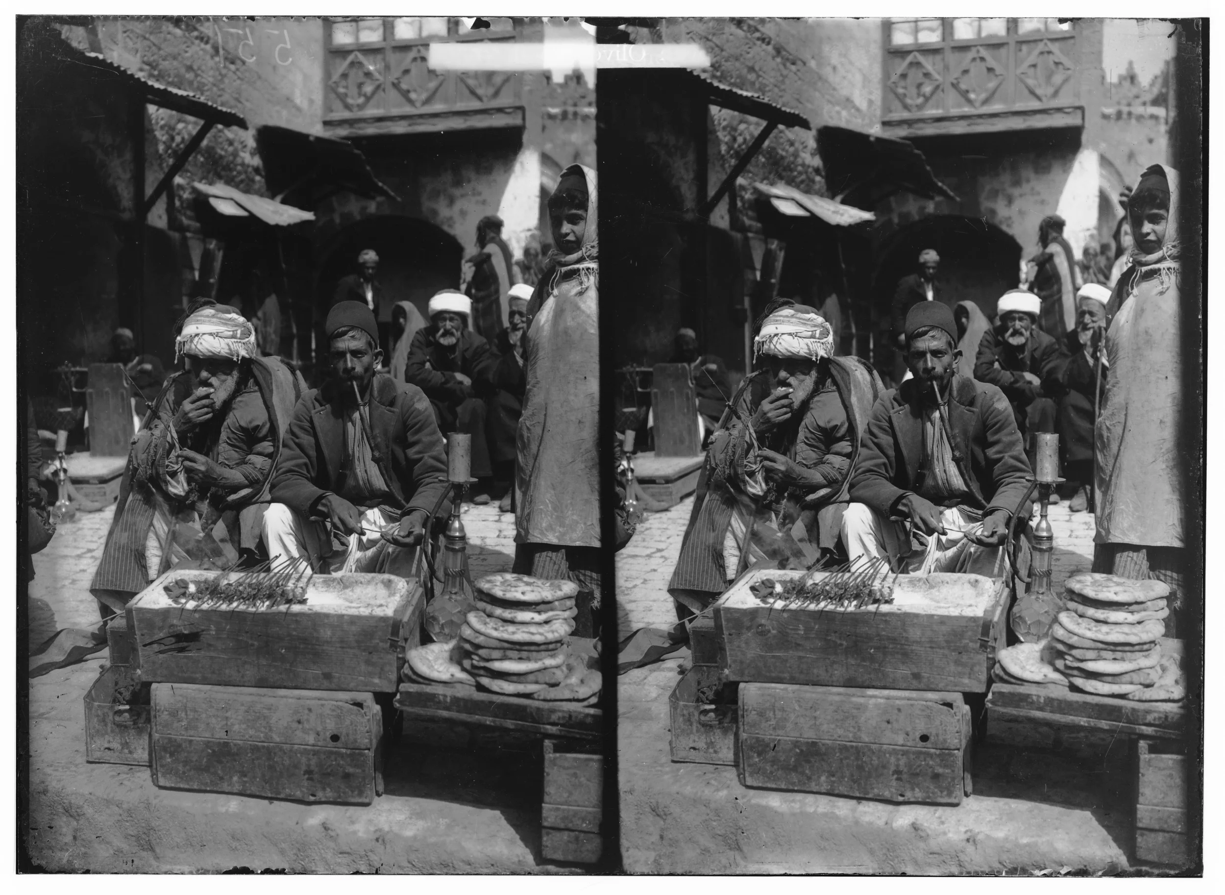 Black and white stereoscopic photograph of street vendors selling bread and food items outdoors, with several men sitting and standing, some smoking, and a woman in traditional attire, in a bustling market scene.