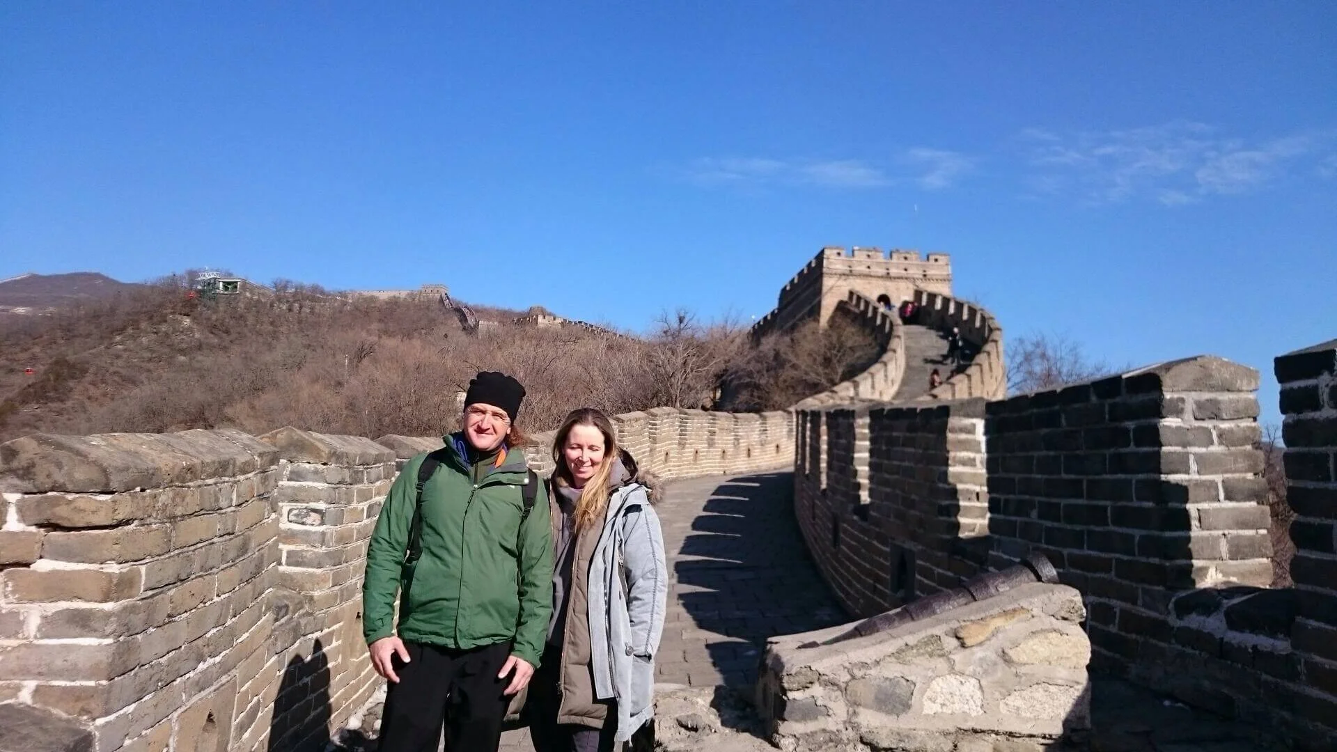 Two people standing on the Great Wall of China with a clear blue sky in the background.