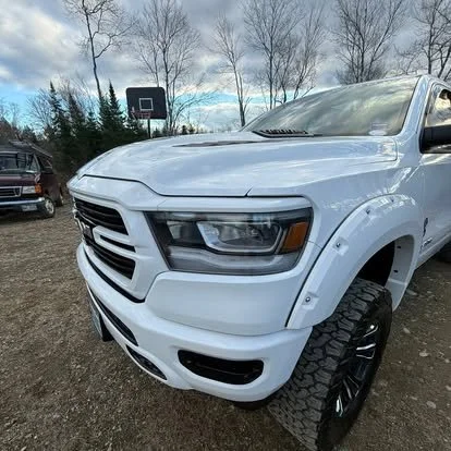 White pickup truck parked outdoors with trees and a basketball hoop in the background.