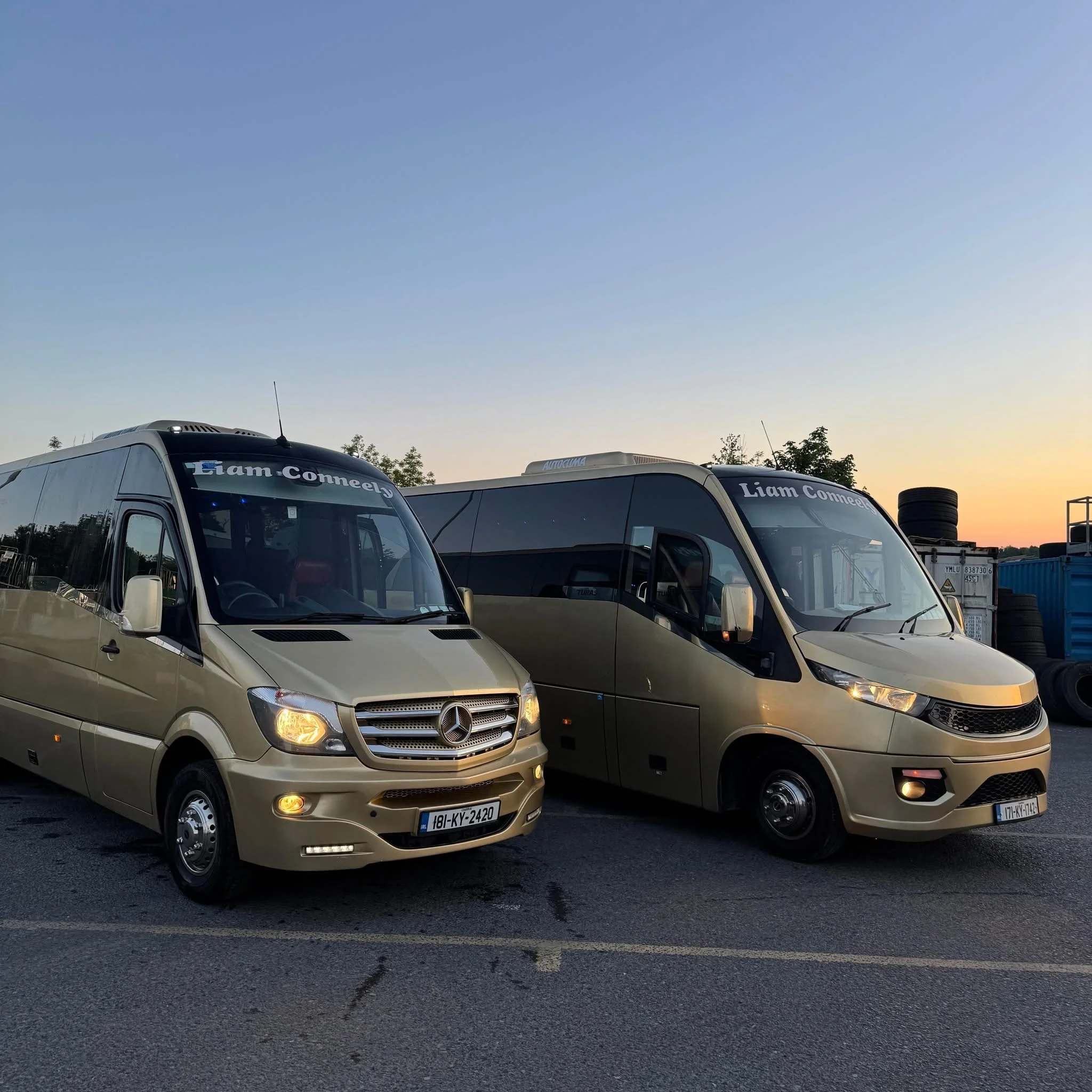A row of parked vans with open parking spaces in the foreground and a clear blue sky during sunset in the background.