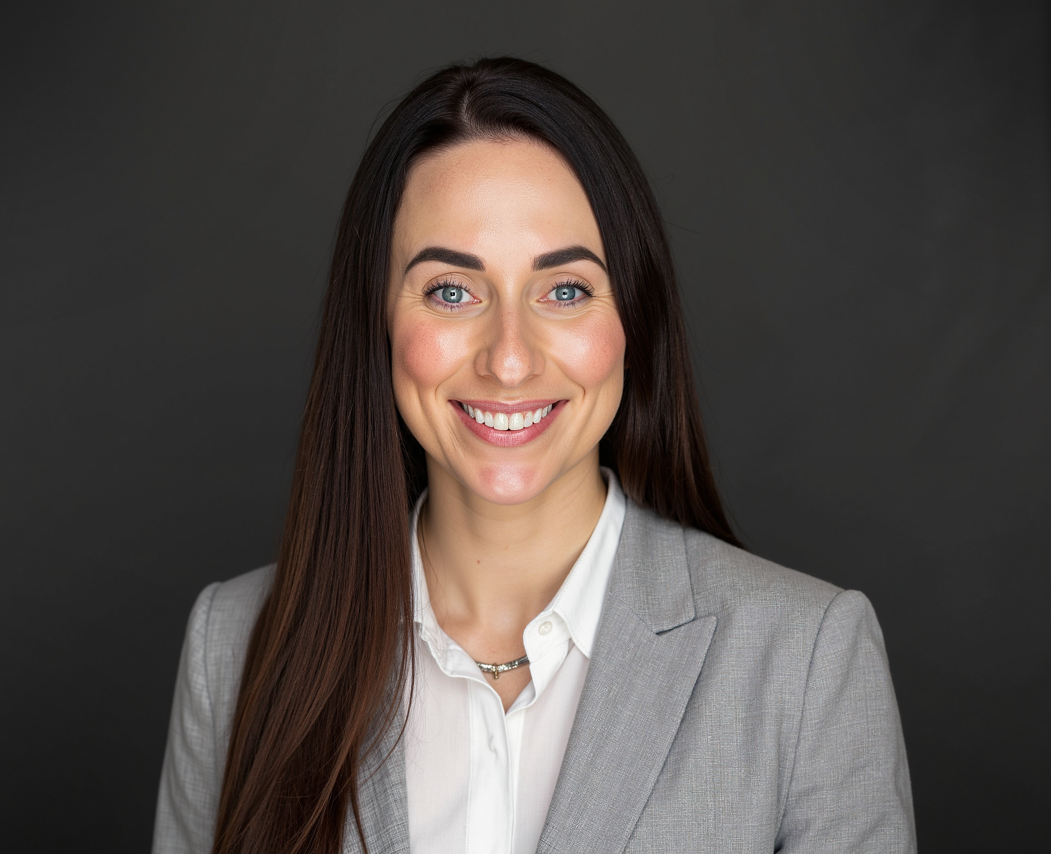 Portrait of Dr. Rebecca Griffith. She has long dark hair, and is wearing a gray blazer and white blouse against a plain dark background.