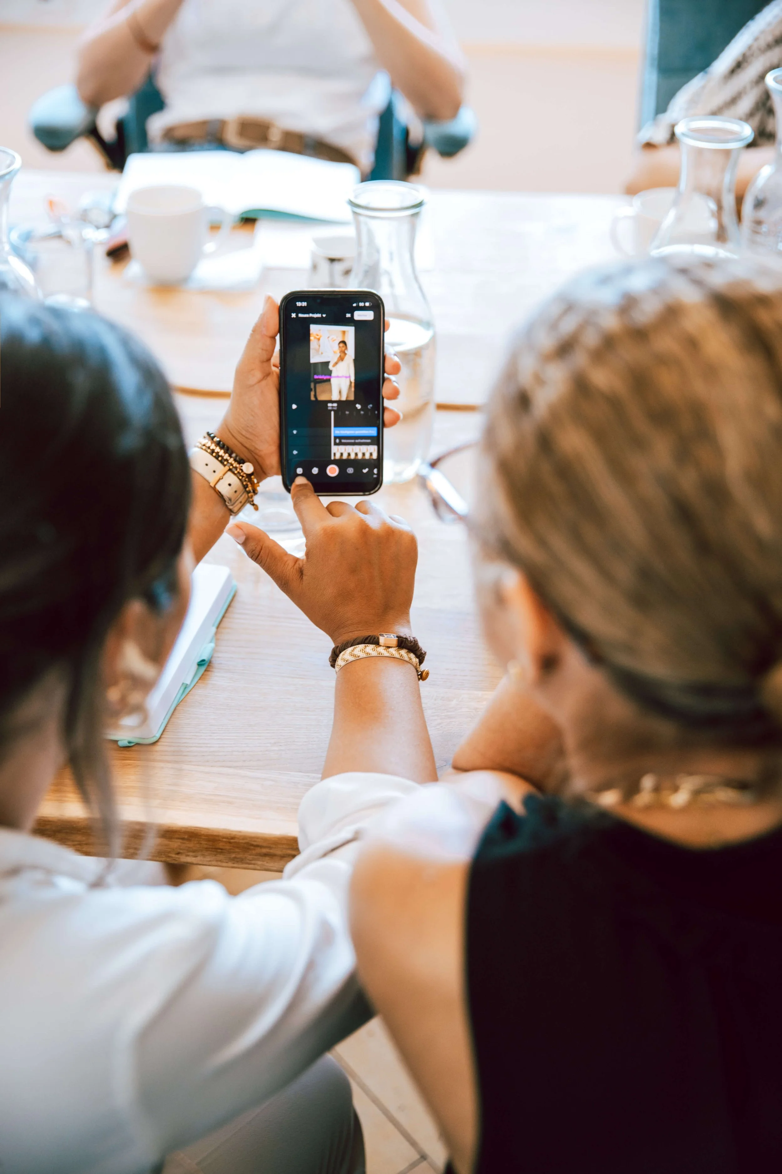 Menschen sitzen um einen Tisch, während eine Person ein Smartphone benutzt, um ein Video oder Foto von einer anderen Person aufzunehmen.