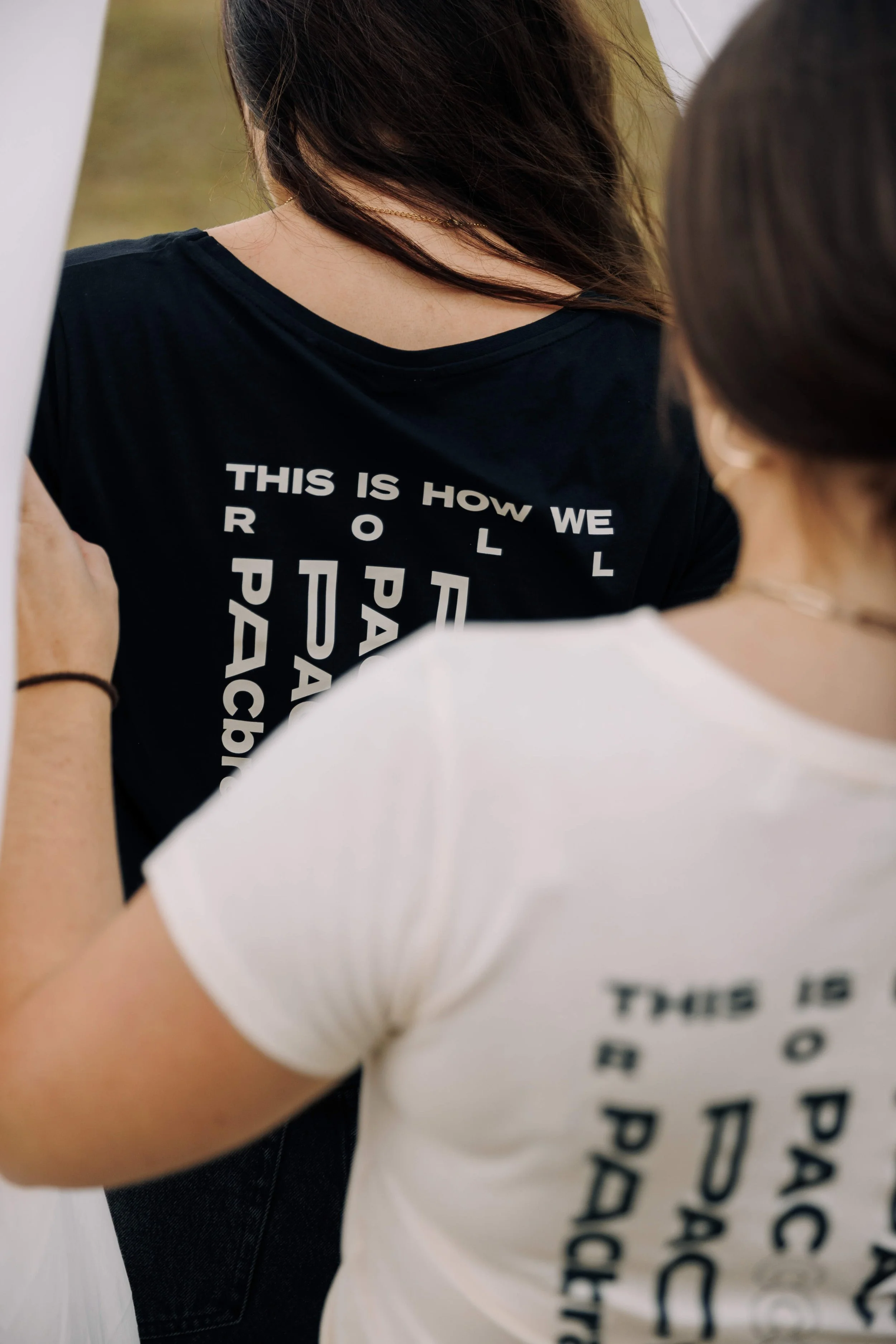 Nahaufnahme von zwei Personen, eine trägt ein schwarzes T-Shirt mit weißen Texten, die sagen 'This is how we roll', die andere trägt ein weißes T-Shirt mit schwarzen Buchstaben.