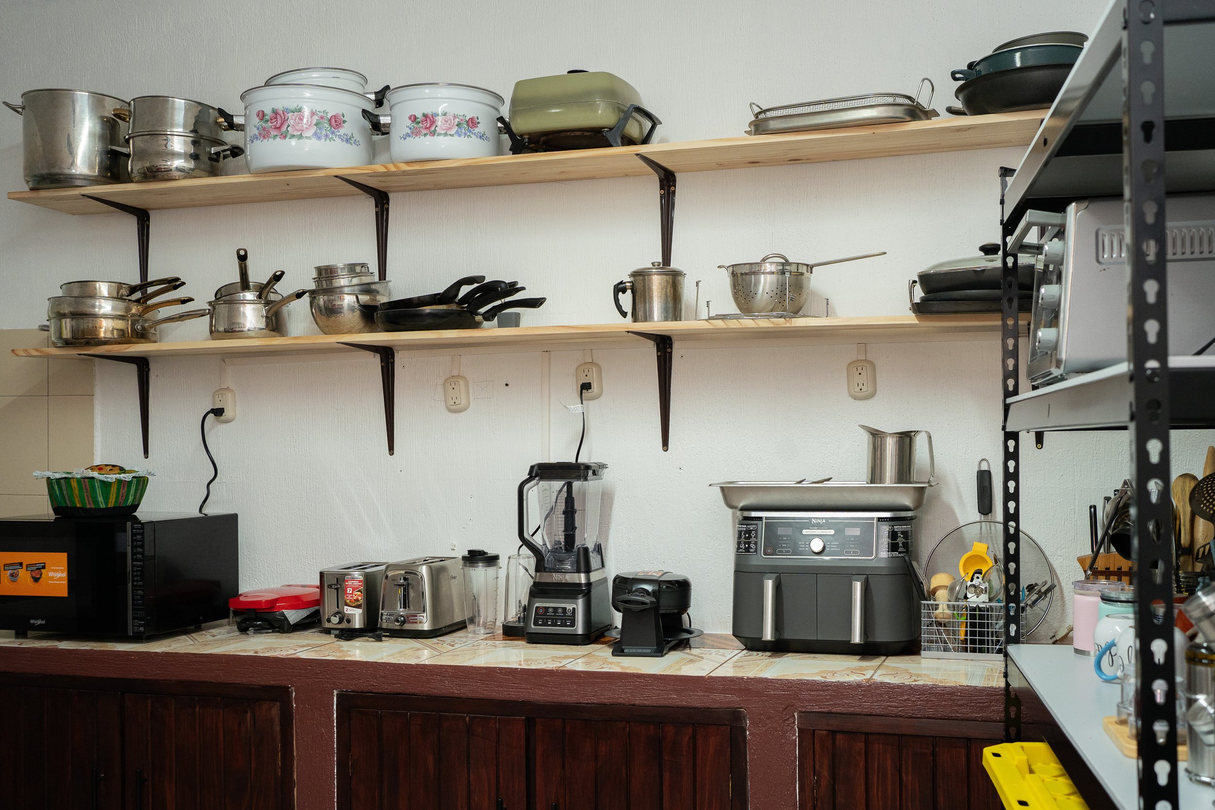 Kitchen shelves with various pots, pans, and kitchen appliances including a blender, toaster, and microwave, on a tiled countertop.