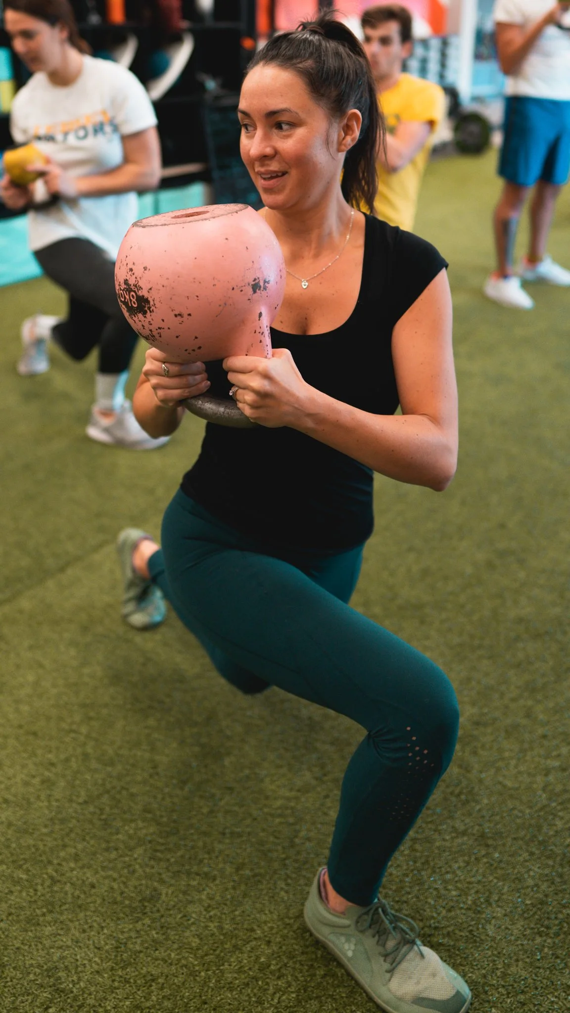 Woman in workout clothes holding a pink kettlebell during exercise class.