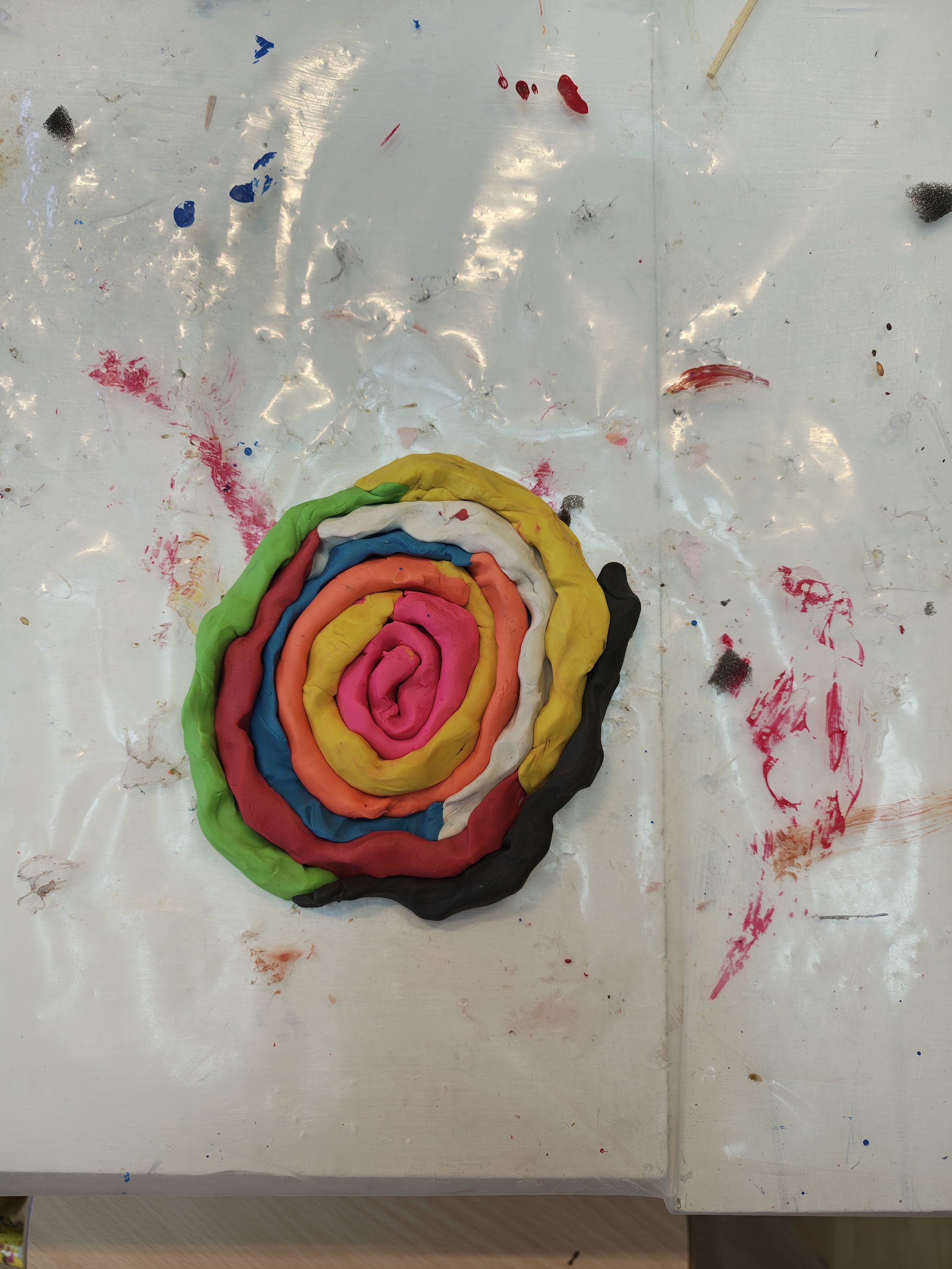 Colorful coiled modeling clay on a white table with paint splatters.
