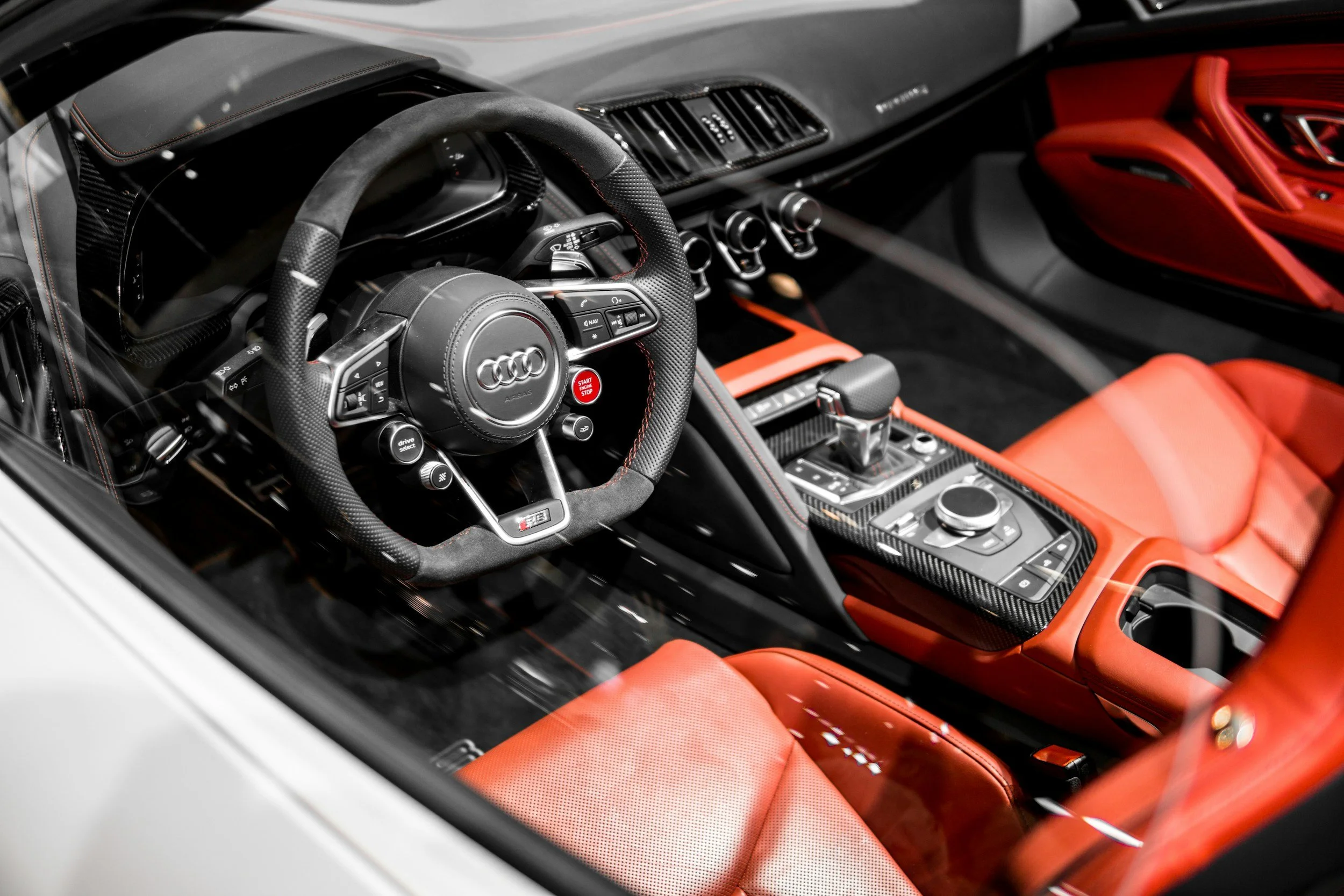 The interior of a luxury sports car with a black steering wheel, red seats, and a modern dashboard with various controls and displays.