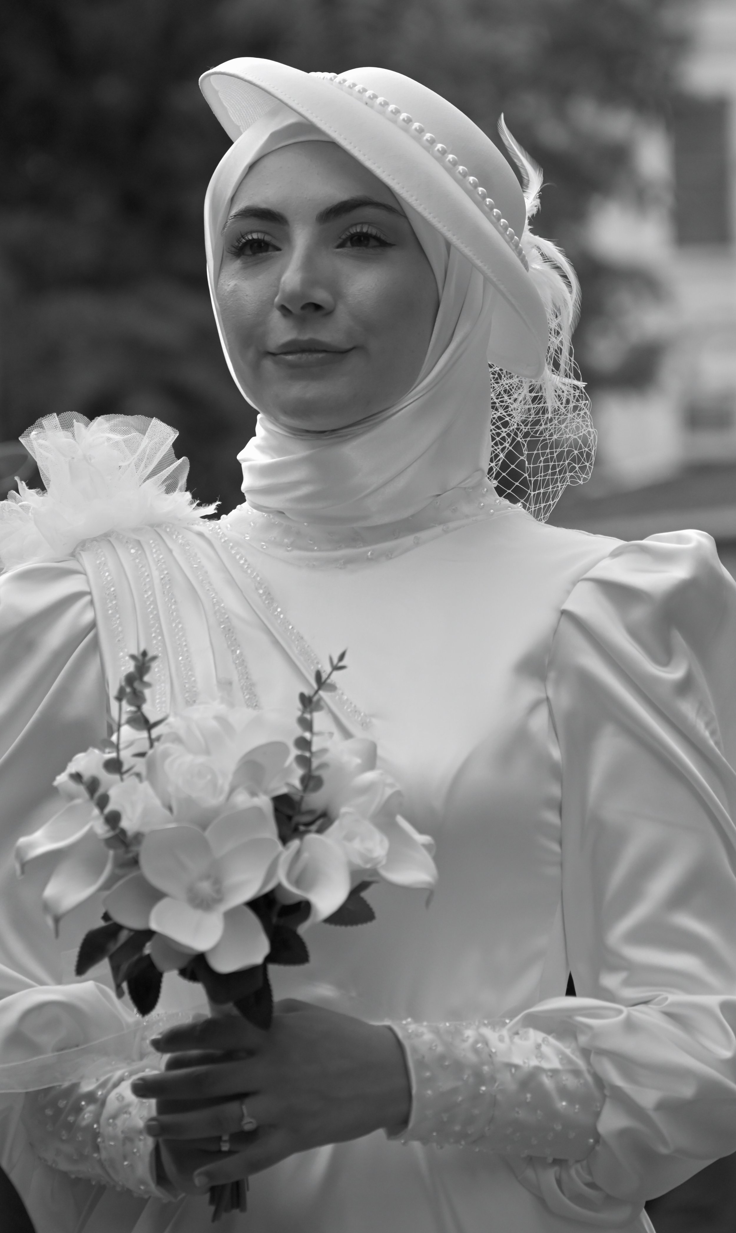 A woman in a white dress and headscarf holding a bouquet of white flowers.