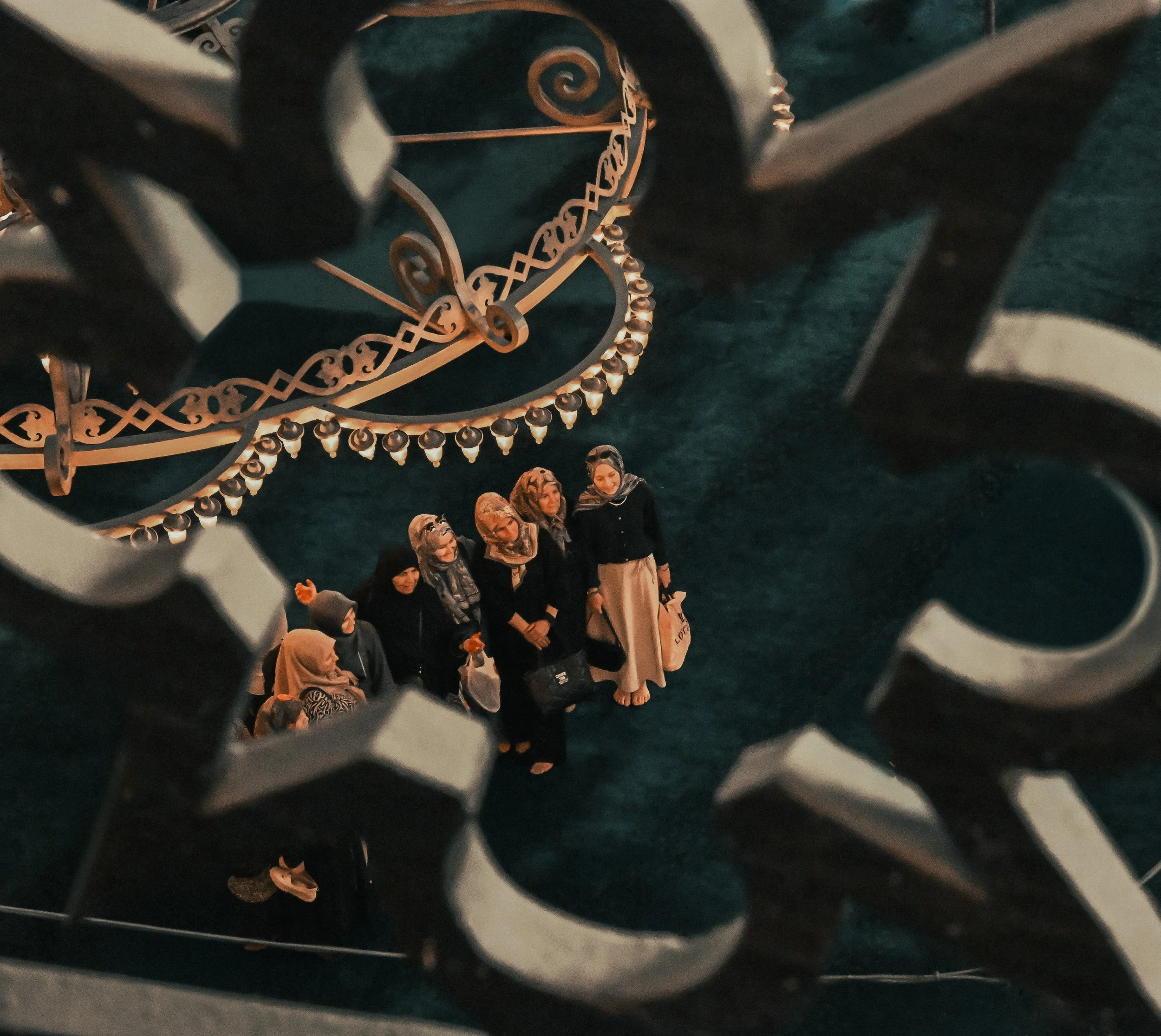 A group of women in headscarves standing together in front of an ornate clock with gold details, viewed through a decorative, circular hole.