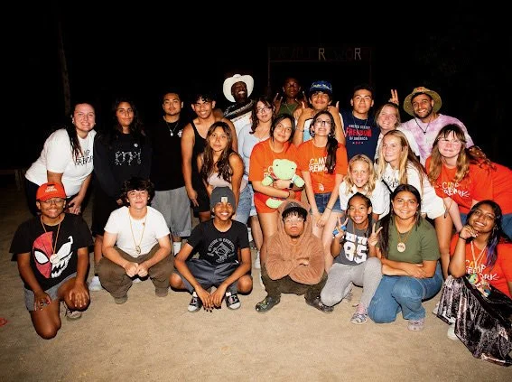 Group of young people and adults posing outdoors at night, some making peace signs and smiling.