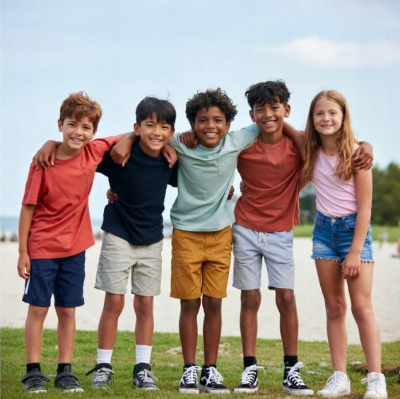 Five kids standing on grass outdoors with arms around each other, smiling at the camera.