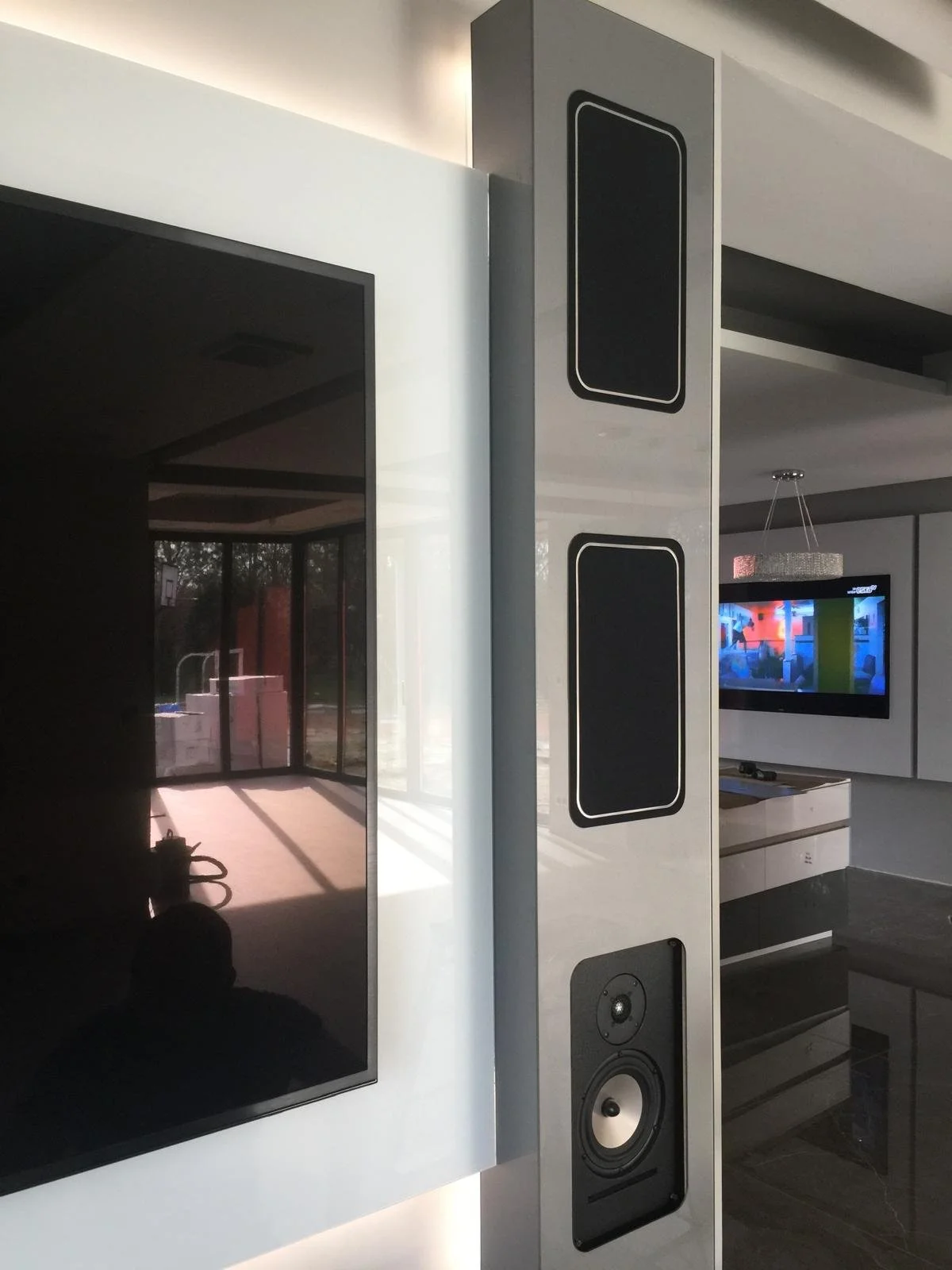 Modern living room with a large flat-screen TV, a tall musical speaker, and a wall-mounted TV displaying colorful abstract art.