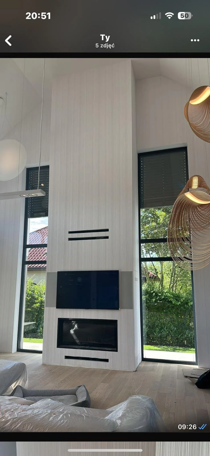 Modern living room with large windows, a wall-mounted TV, a fireplace, and contemporary lighting fixtures.