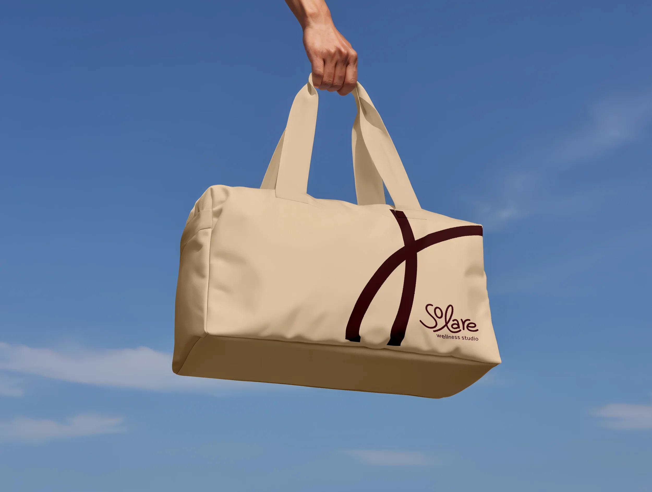A white tote bag with a logo that reads 'Solare wellness studio' is being held up against a blue sky with some clouds.