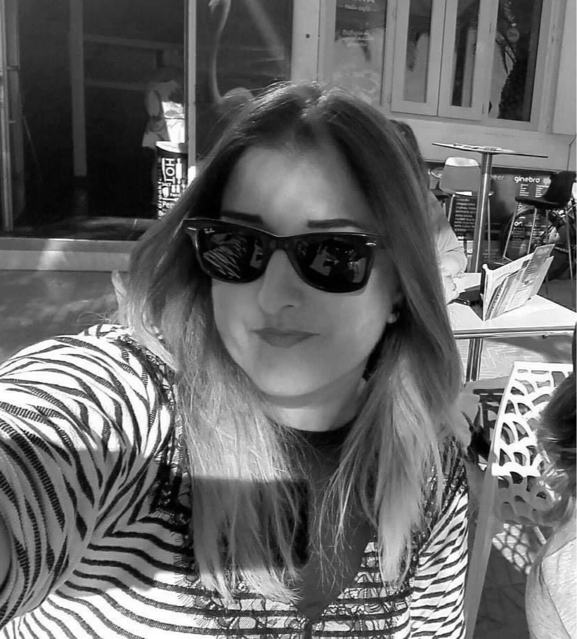 Young woman wearing sunglasses and a zebra-print top taking a selfie in a casual outdoor setting.