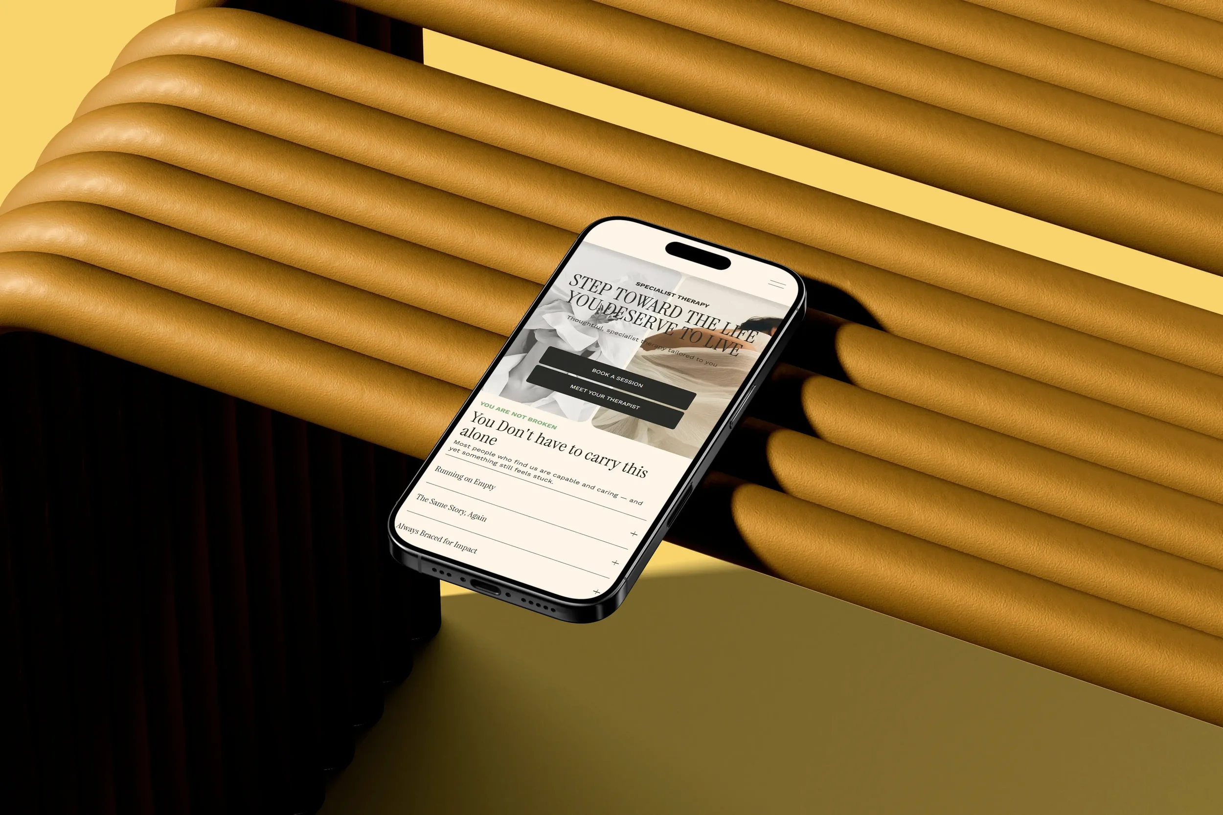 A smartphone displaying a therapy website in a modern setting with decorated yellow and black cushions.