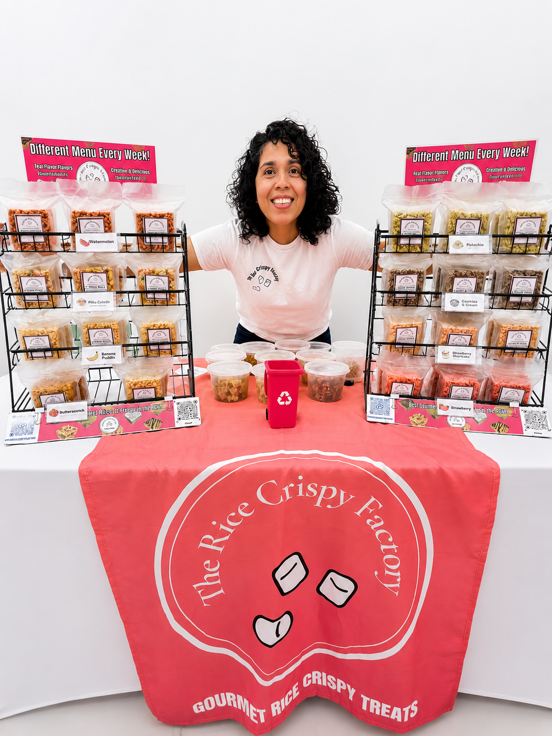 Woman smiling at a rice crispy treat booth with colorful packaged treats on display at the table and signs promoting new flavors.