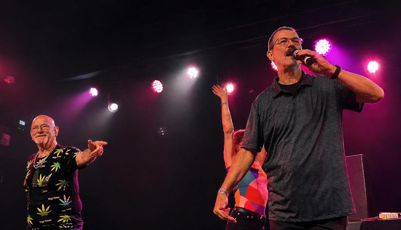 The artist 'story.' sings on stage while a woman dances behind him. Off to one side, Pete (of Pete and Bas) looks on, pointing and smiling.