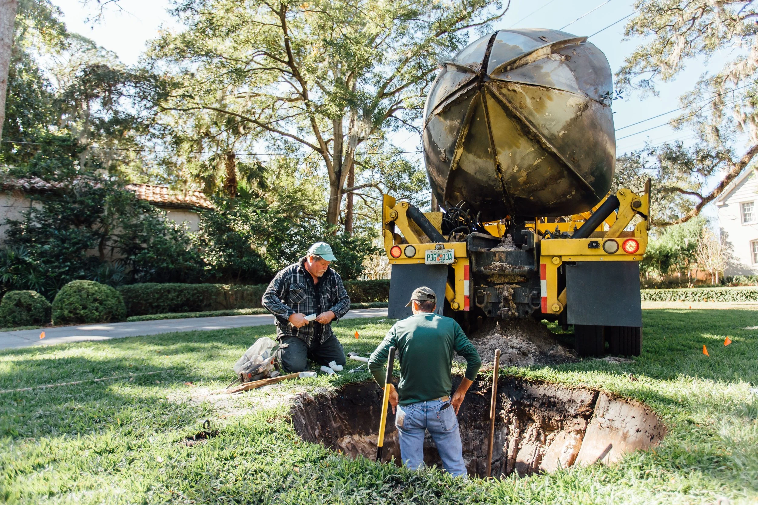 Workers performing underground utility line work using a large vacuum excavation truck on a residential street.