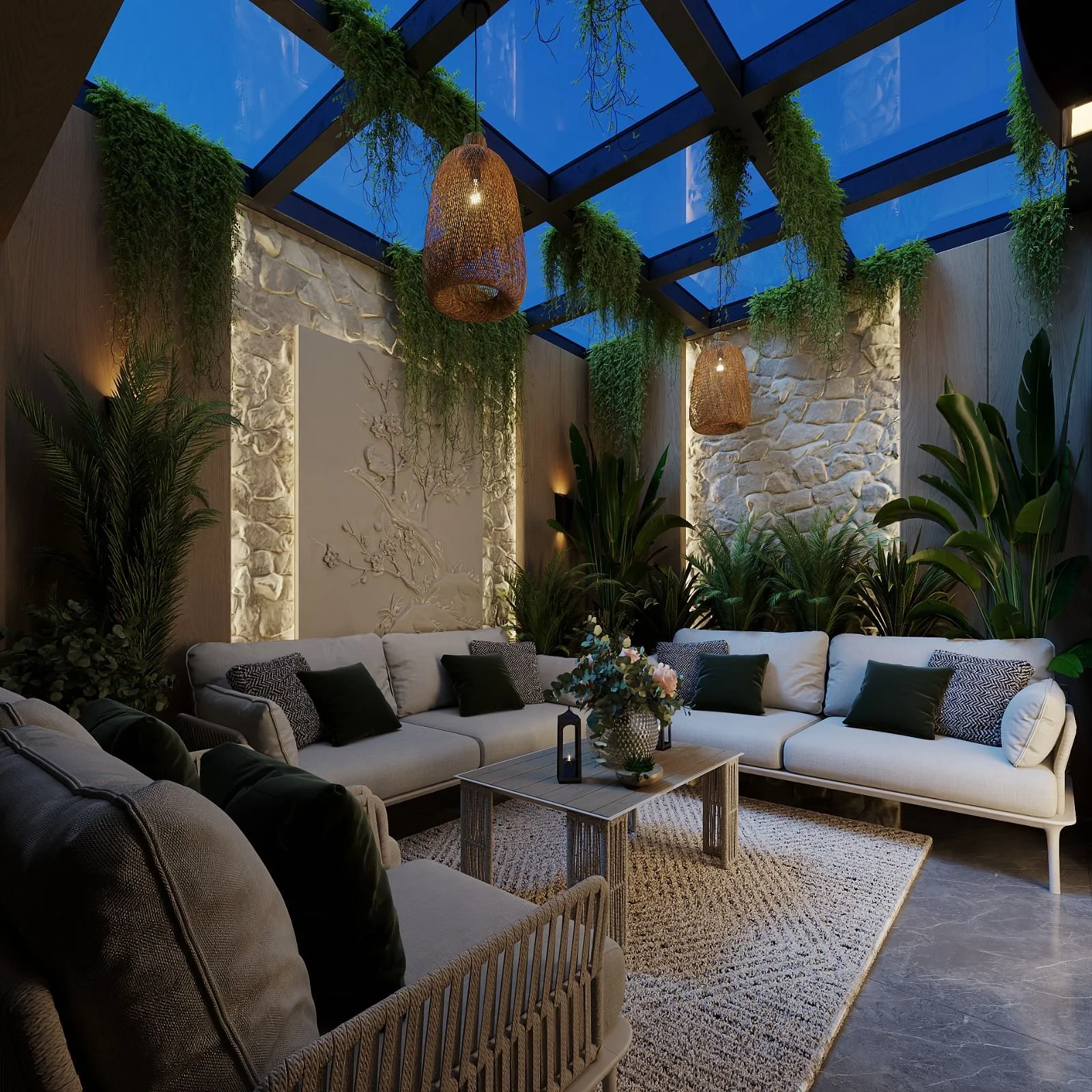A cozy indoor living room with a large white sectional sofa decorated with black and gray pillows. A wooden coffee table with a flower arrangement, lantern, and decorative objects is centered on a beige rug. The room features a textured stone wall, tall green plants, and hanging wicker lamps. The ceiling is made of glass panels with green plants hanging around the edges, allowing a view of a partly cloudy sky.