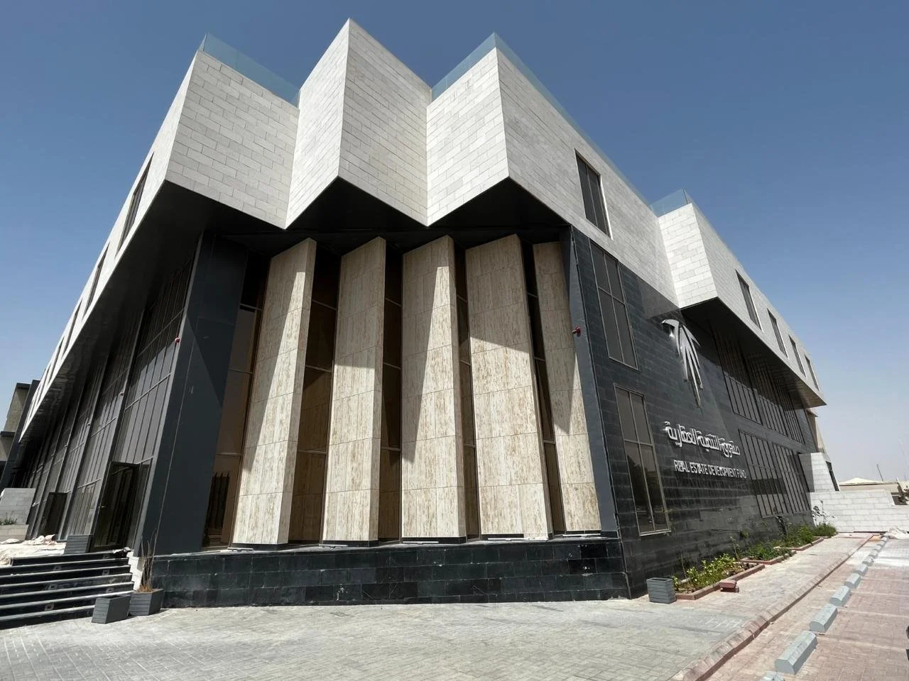 Modern multi-story building with black and light-colored exterior, large windows, and a sign indicating it is a real estate development office.