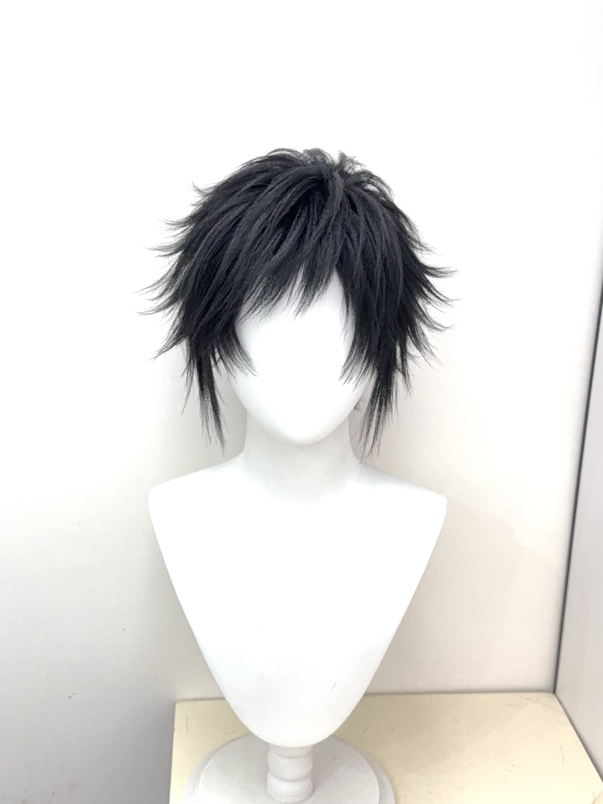 White mannequin head with black, spiky, layered wig against a plain white and beige background.
