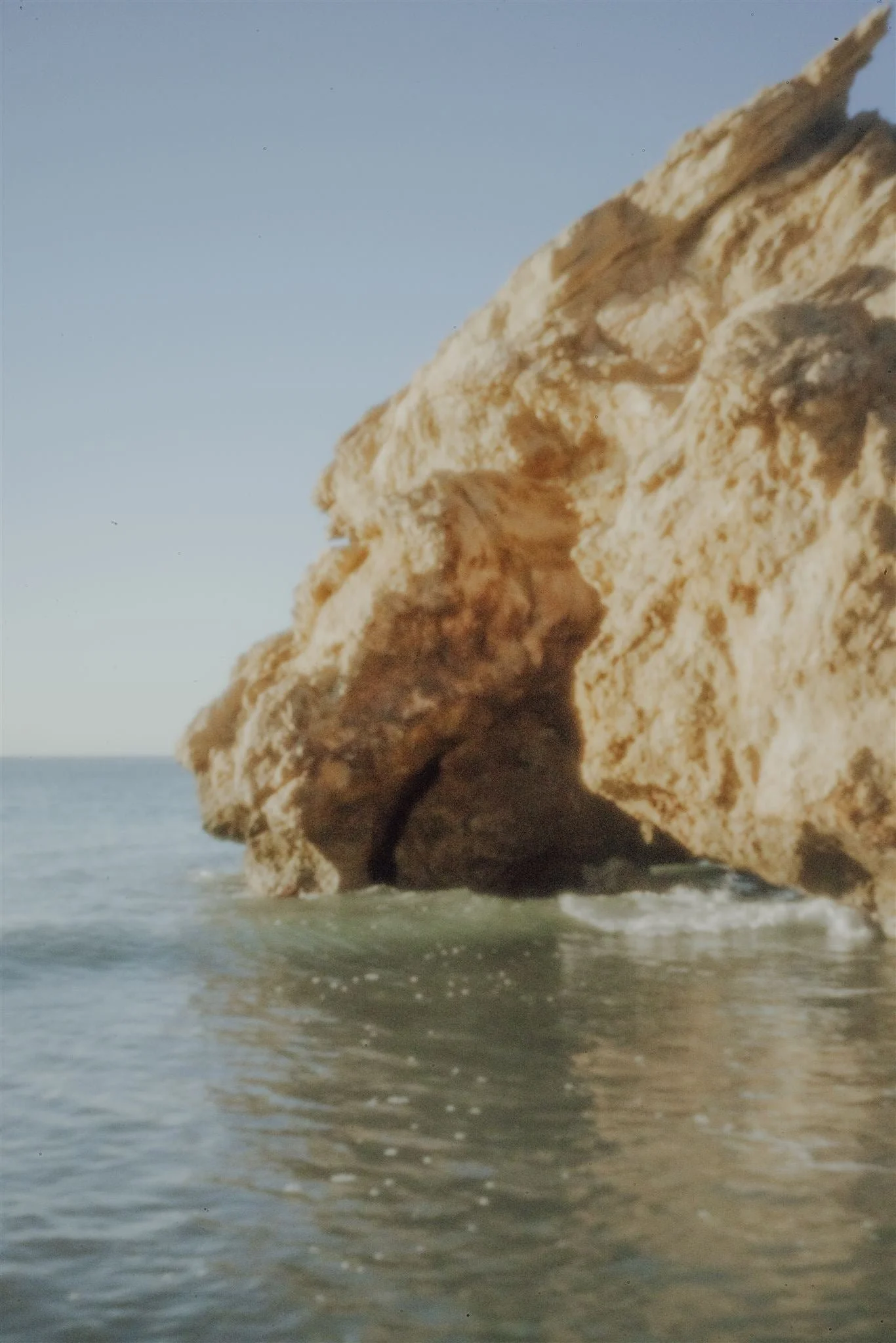 Große Felsformation am Strand mit Wasser und Himmel im Hintergrund.