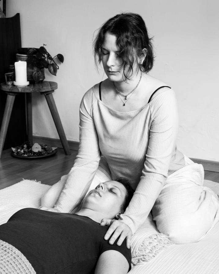 Schwarz-weiß-Foto einer jungen Frau, die beim Energie-Arbeiten bei einem Mann sitzt, der auf dem Boden liegt mit geschlossenen Augen.