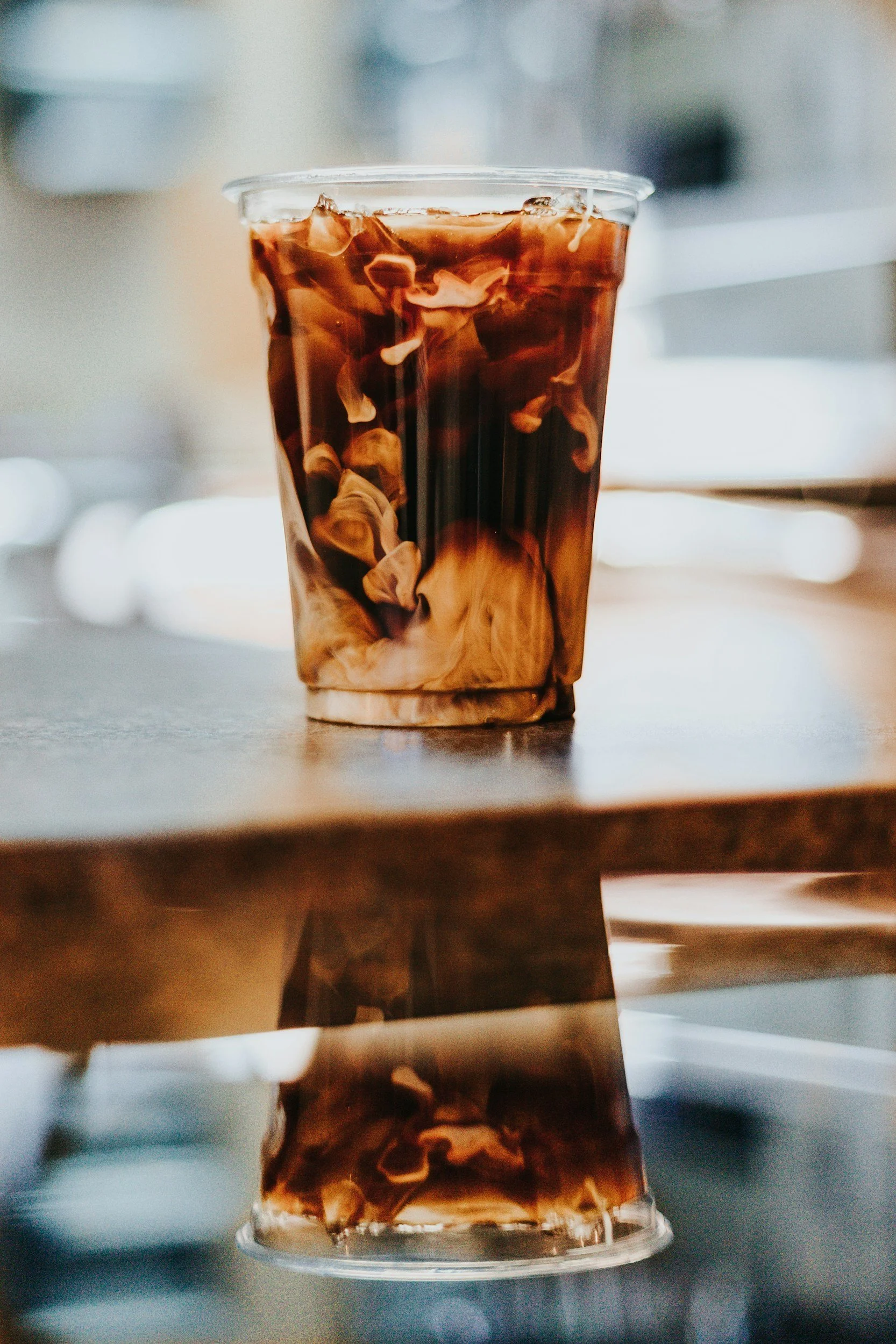 A clear plastic cup filled with iced coffee with cream swirling inside.