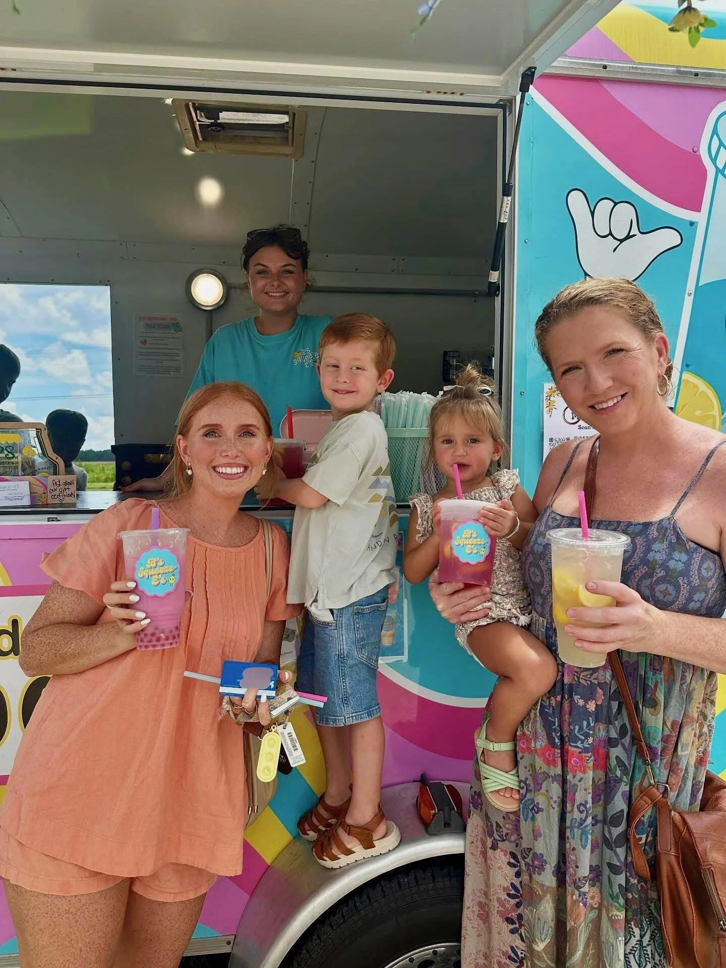 People enjoying smoothies at an ice cream truck on a sunny day.