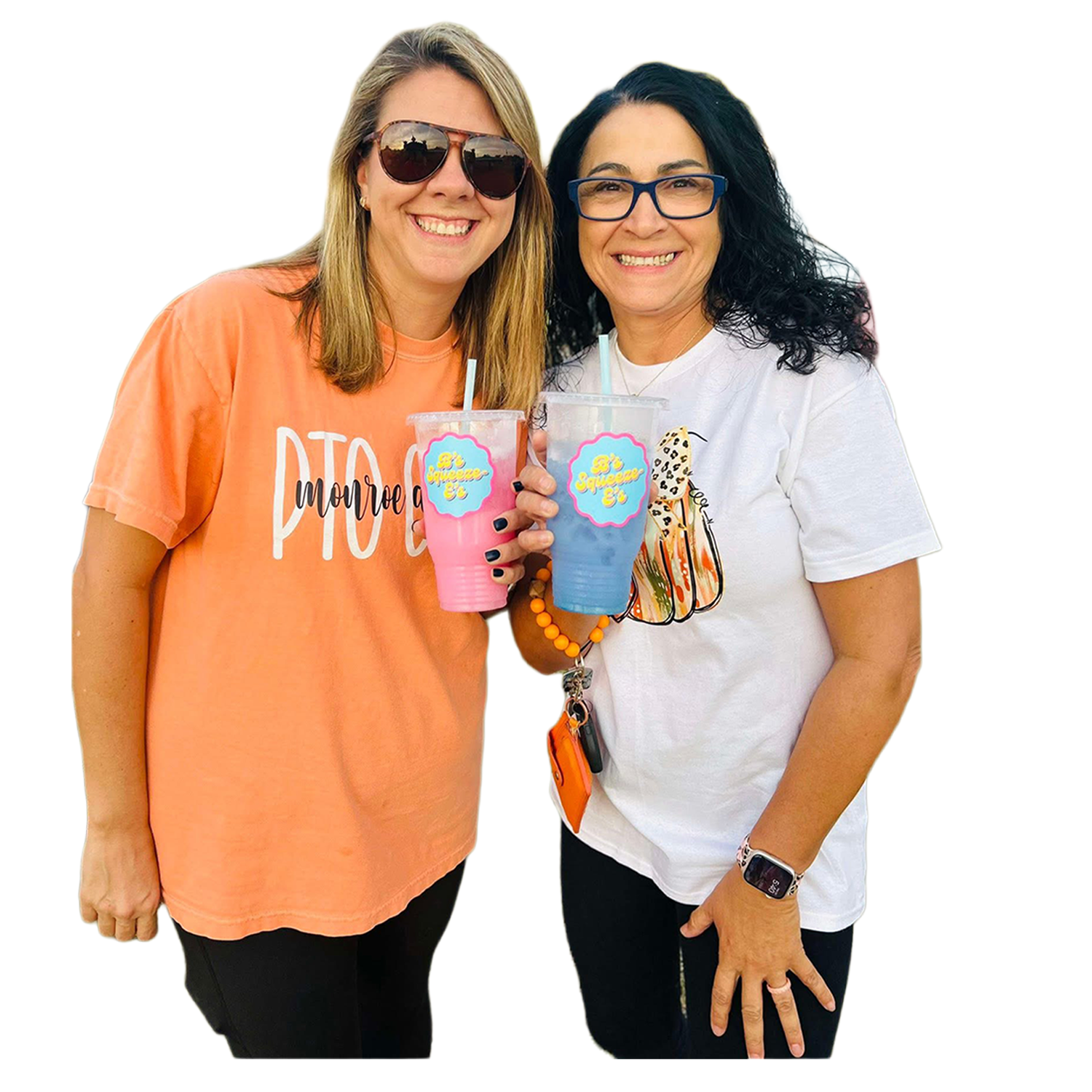 Two women smiling and holding up colorful drinks in clear cups with straws, standing close together against a plain white background.