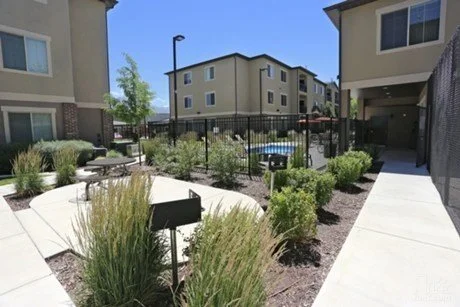 Apartment complex courtyard with plants, a fence, and sitting areas under a clear blue sky.