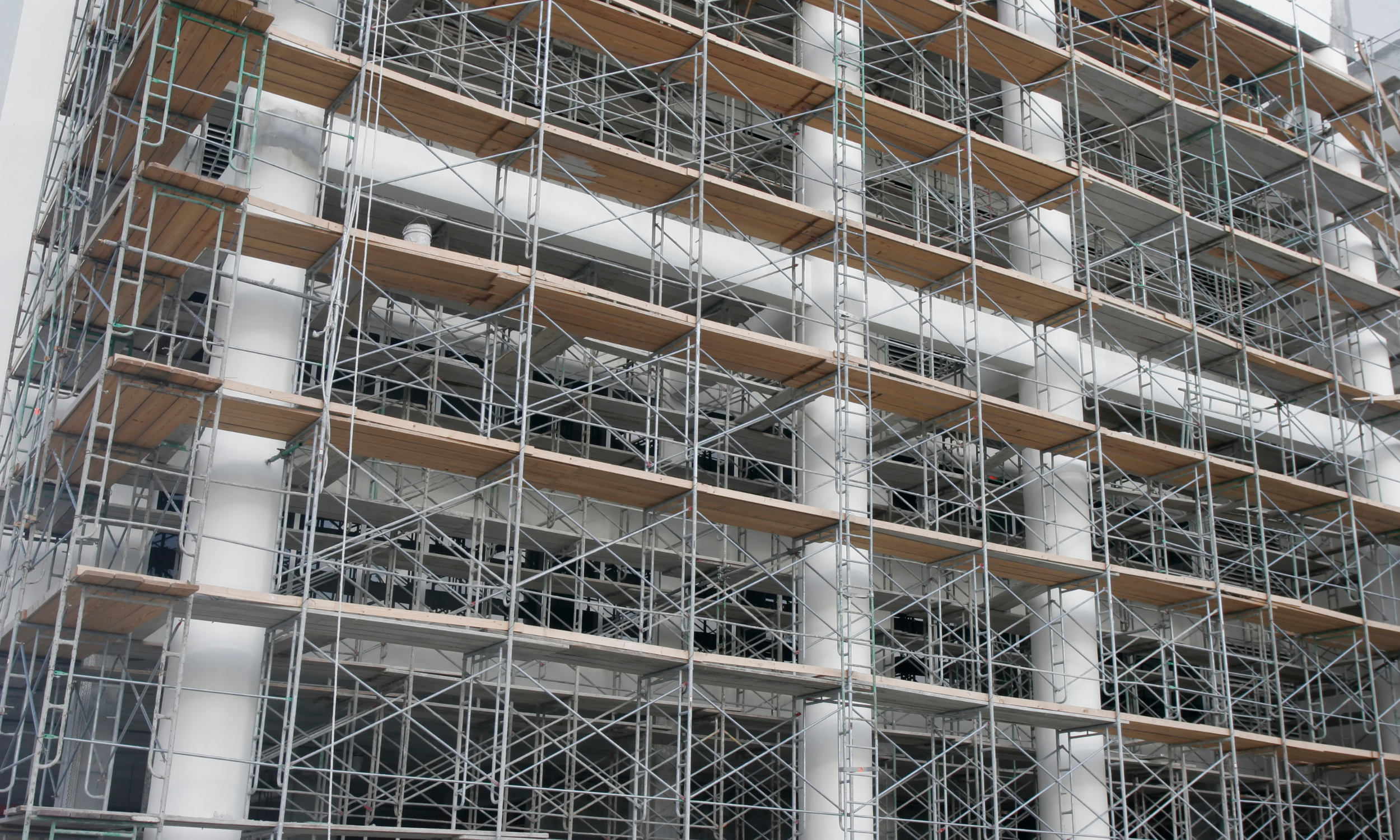 Exterior of a building under construction covered in metal scaffolding with wooden planks