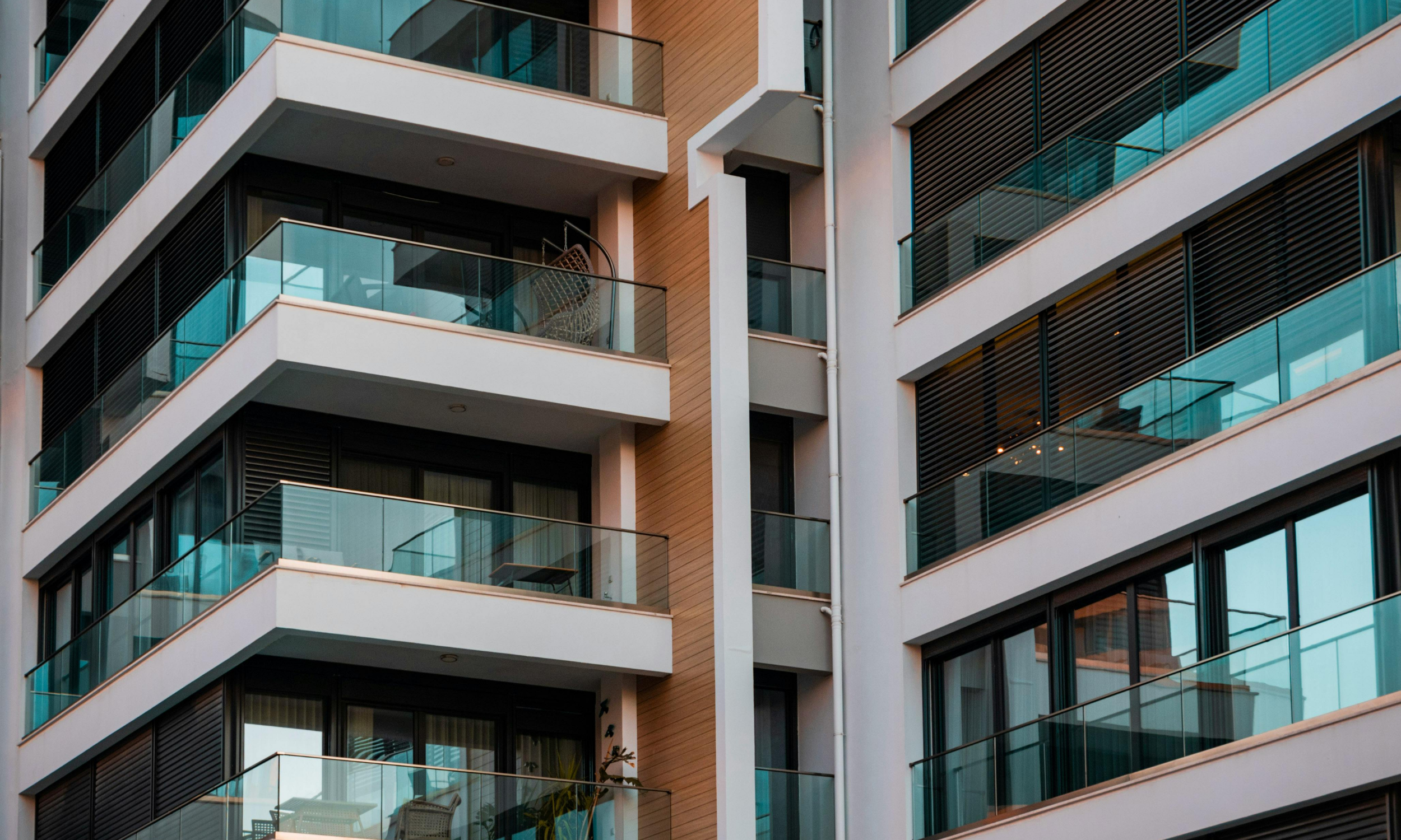 Close-up view of a modern multi-story apartment building with glass balconies and black window shutters