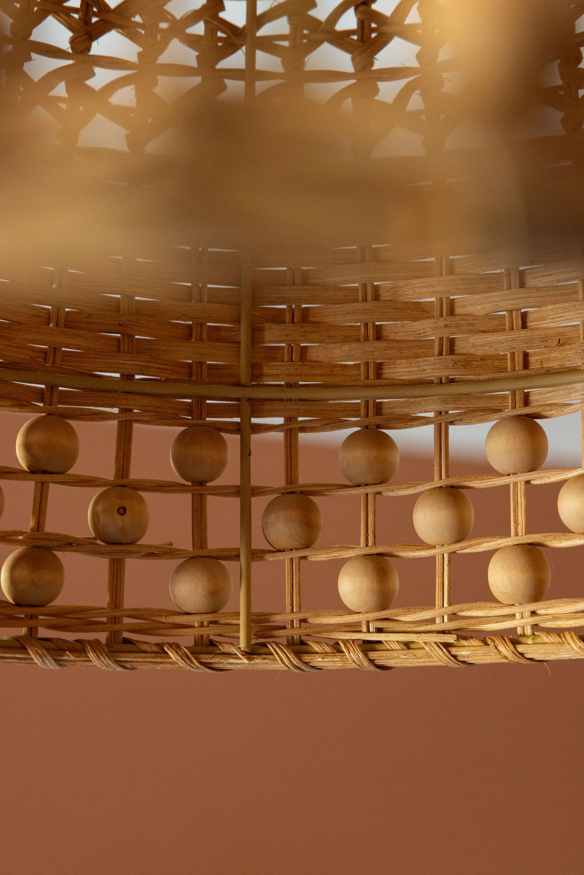 Close-up view of a wicker pendant light with wooden beads hanging from it against an orange wall.