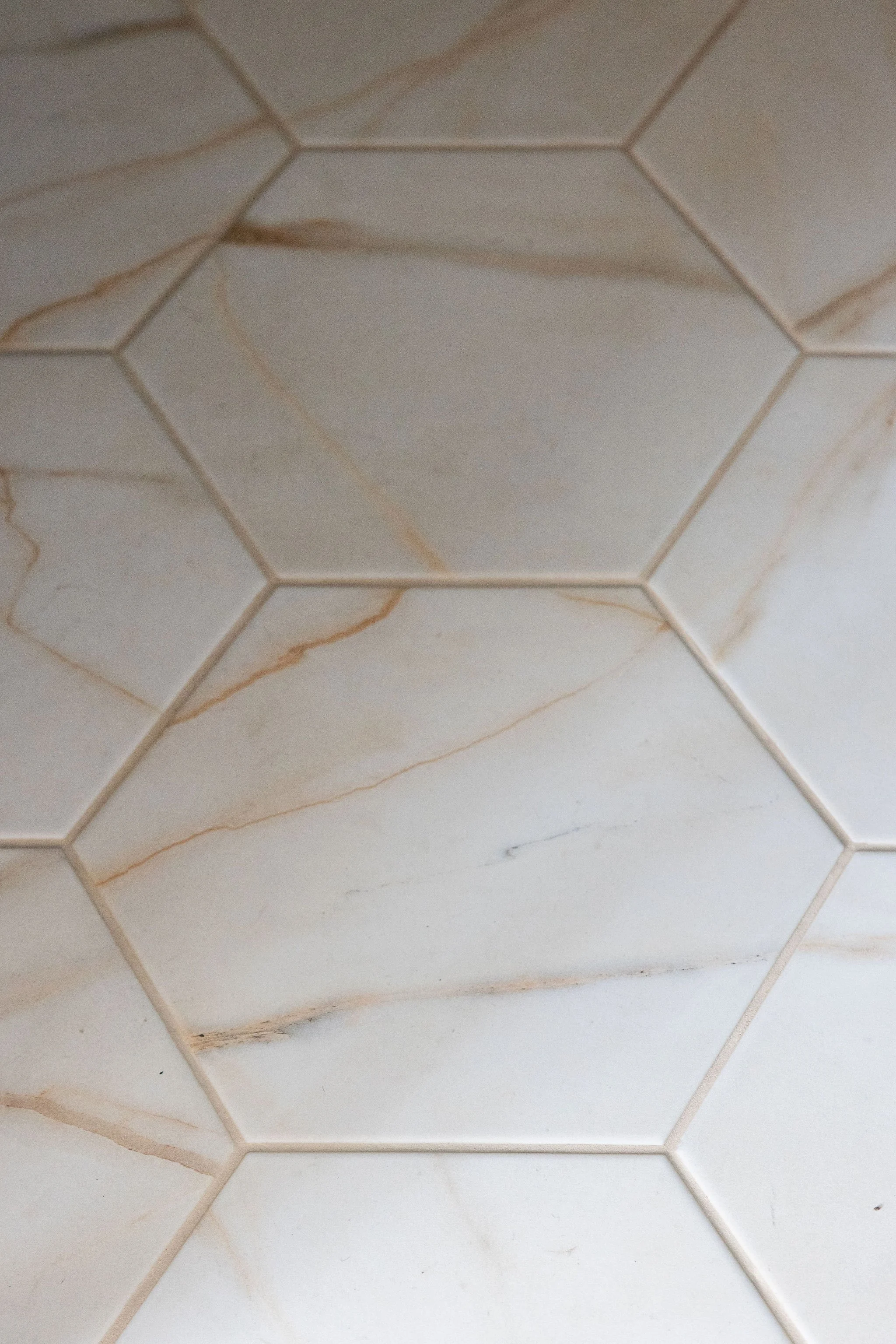 Close-up of white tiles with beige and brown veining, arranged in a hexagonal pattern on a wall or ceiling.