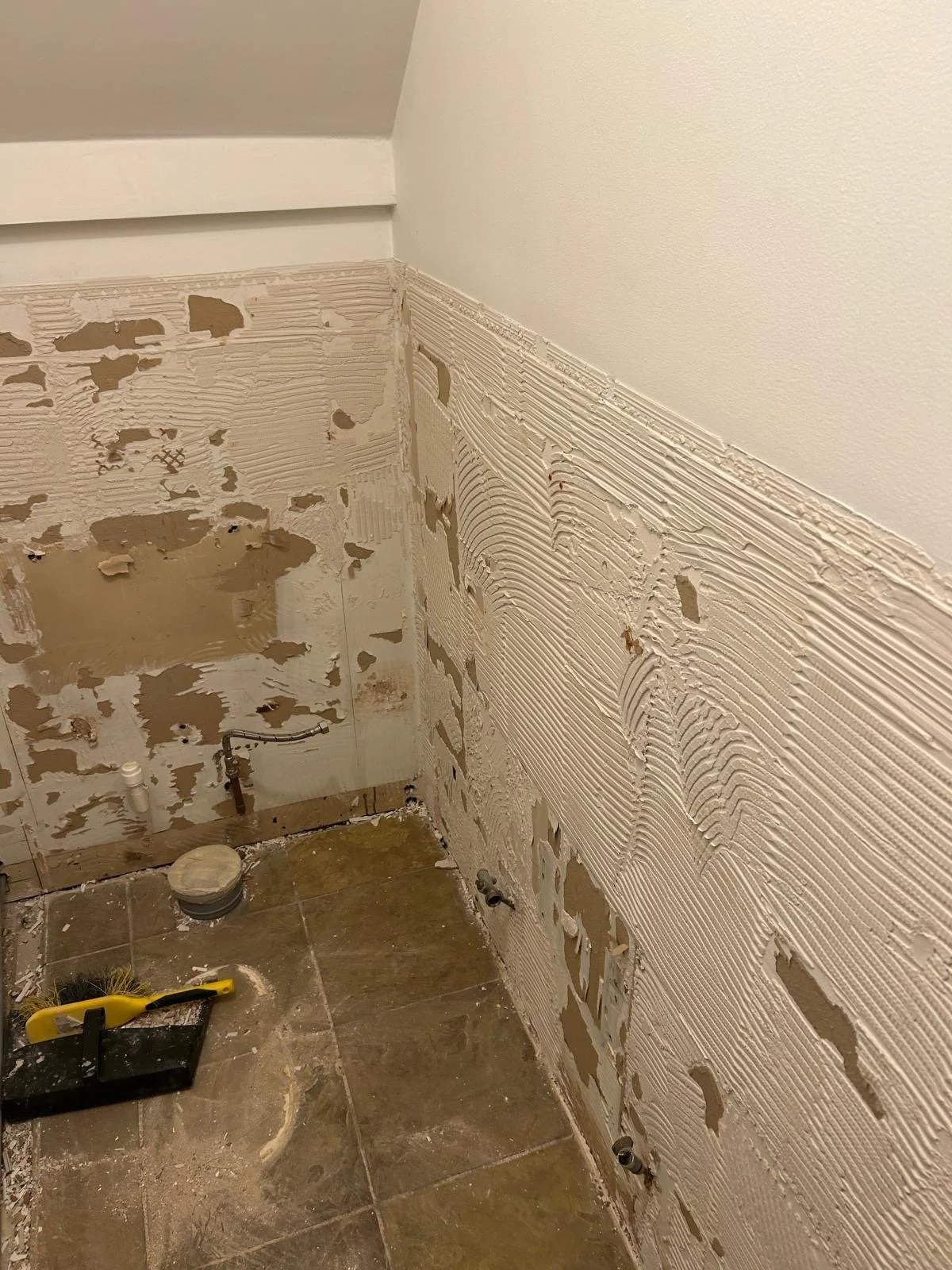Partially renovated bathroom with exposed wall and plumbing, and tile floor, during construction or remodeling.