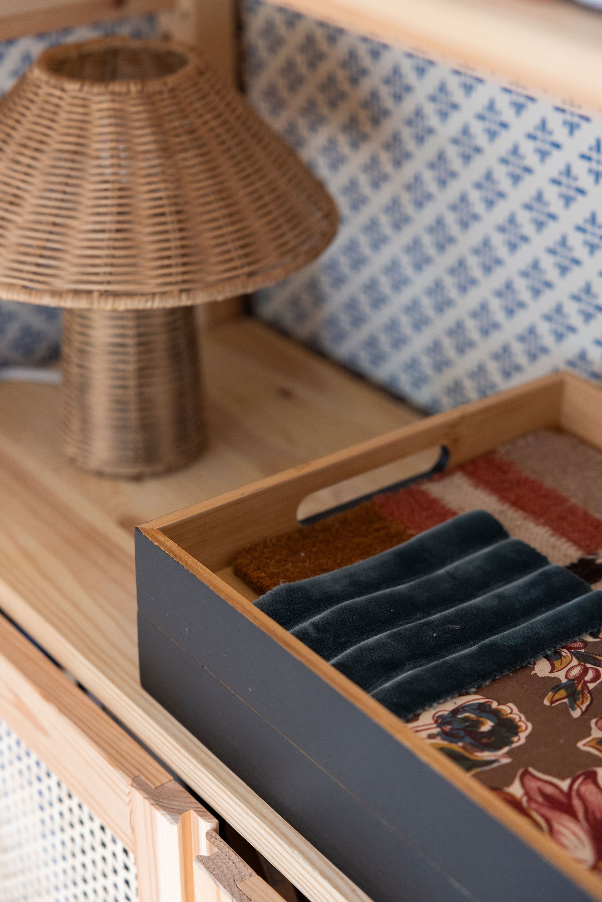 Close-up of a wooden tray with fabric swatches, and a rattan lamp in the background.