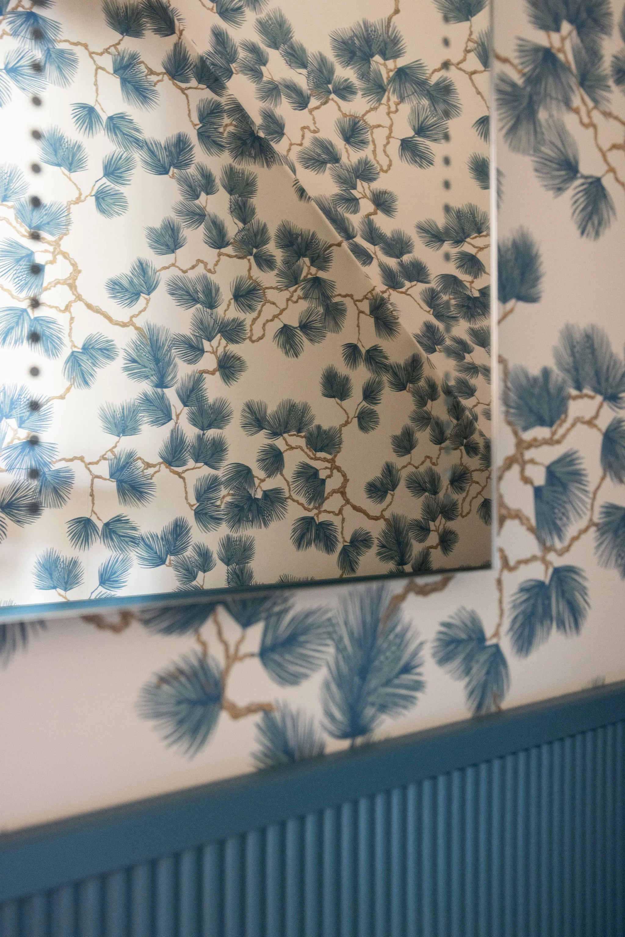 Close-up of a decorative box with a floral pattern of blue and beige branches and leaves, with a reflective mirror inside showing the pattern from a different angle.