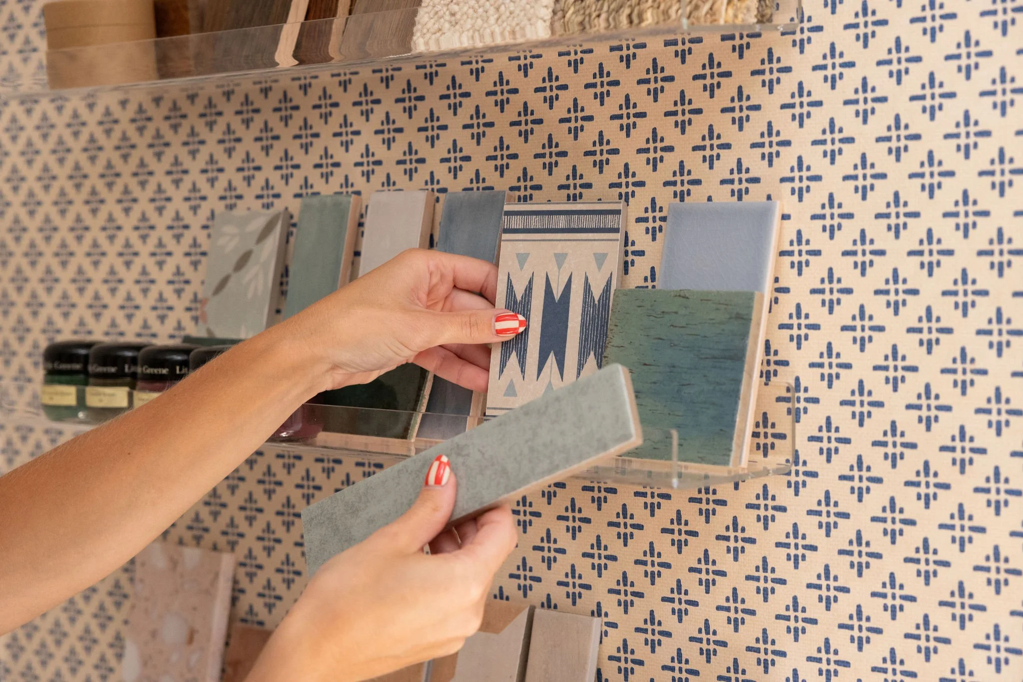 Person holding sample tiles with different patterns in front of a wall decorated with patterned tiles.