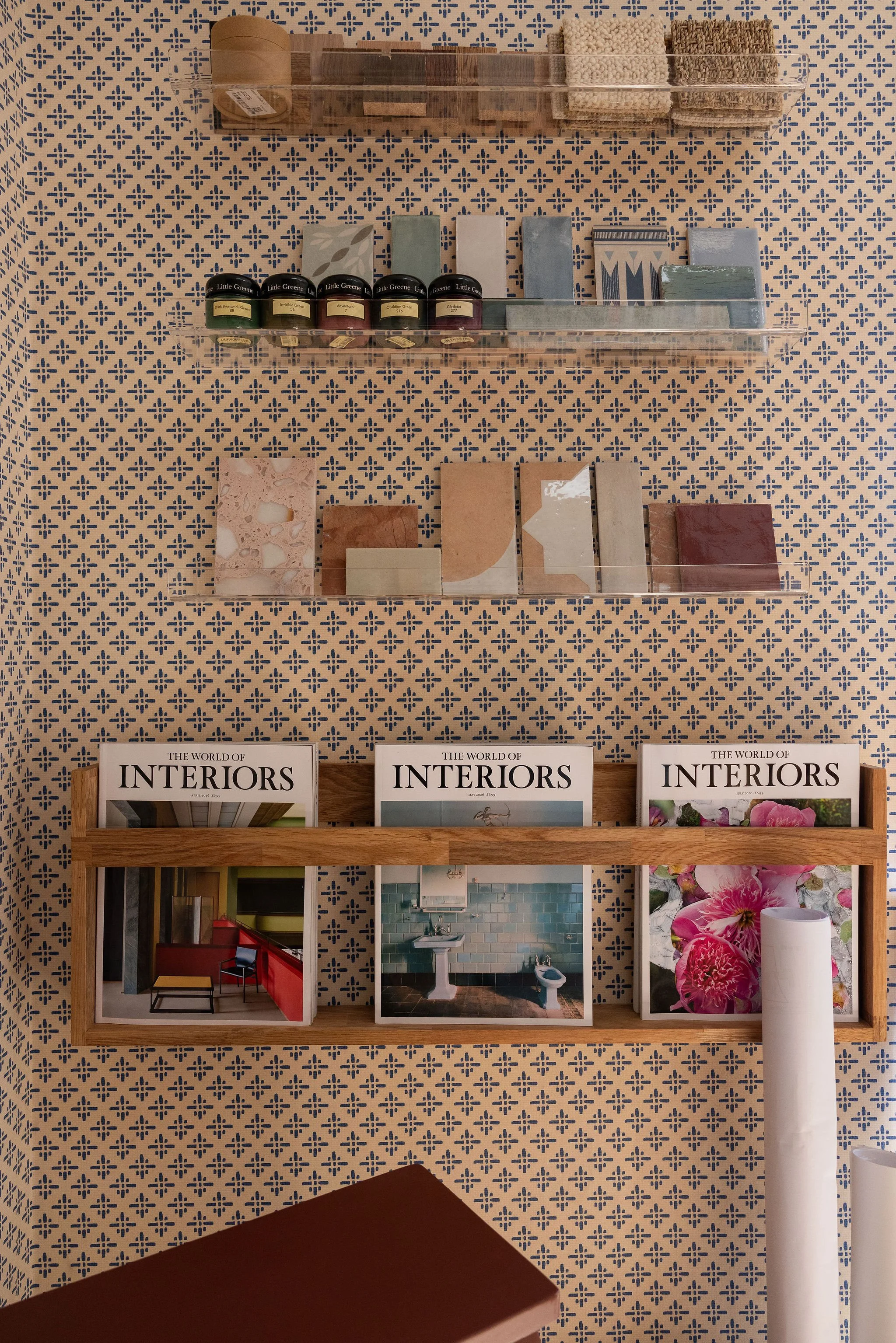 Display of interior design books, color swatches, and paint samples mounted on a wall with patterned wallpaper.